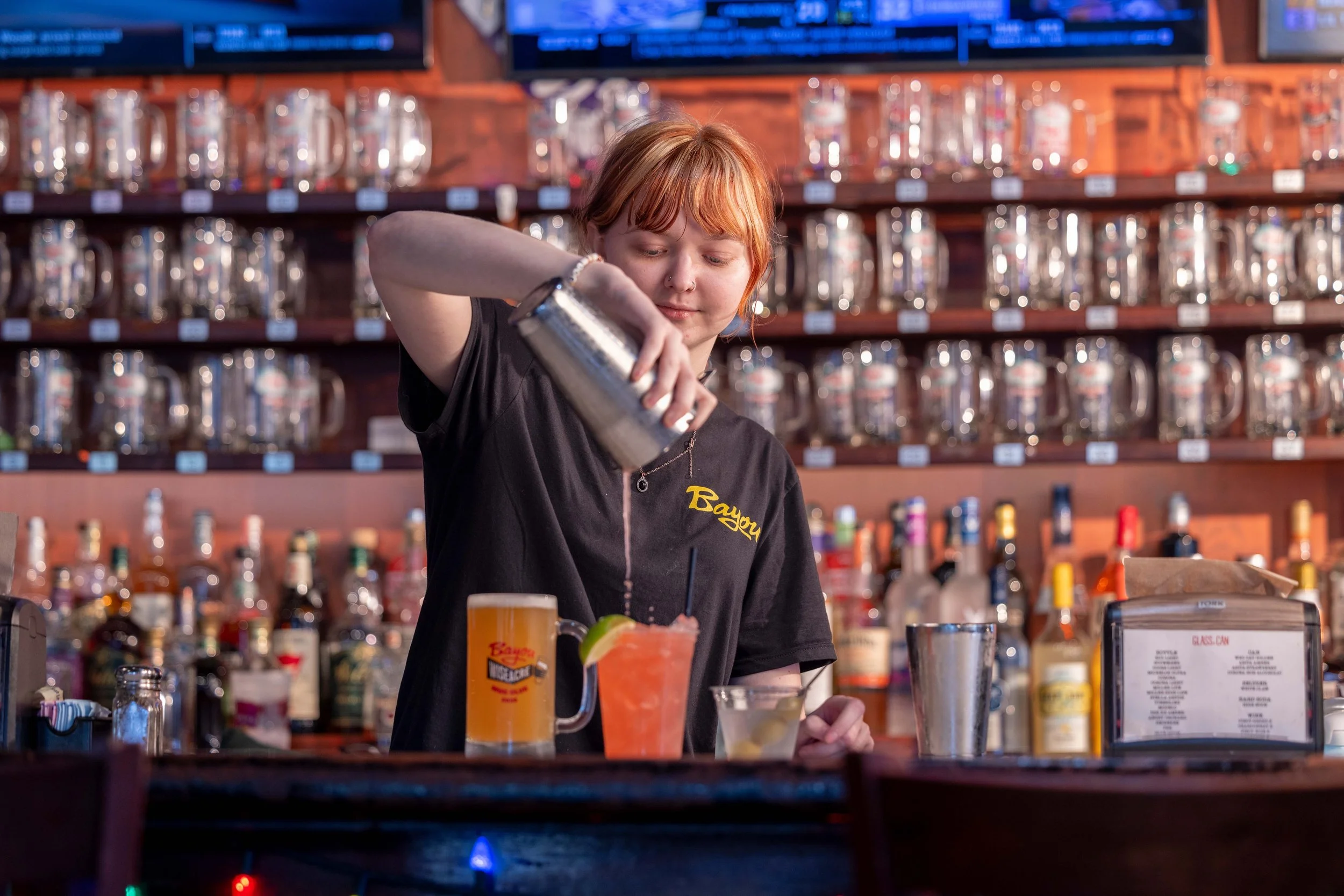 Bartender pouring drinks from cocktail shaker into glass.