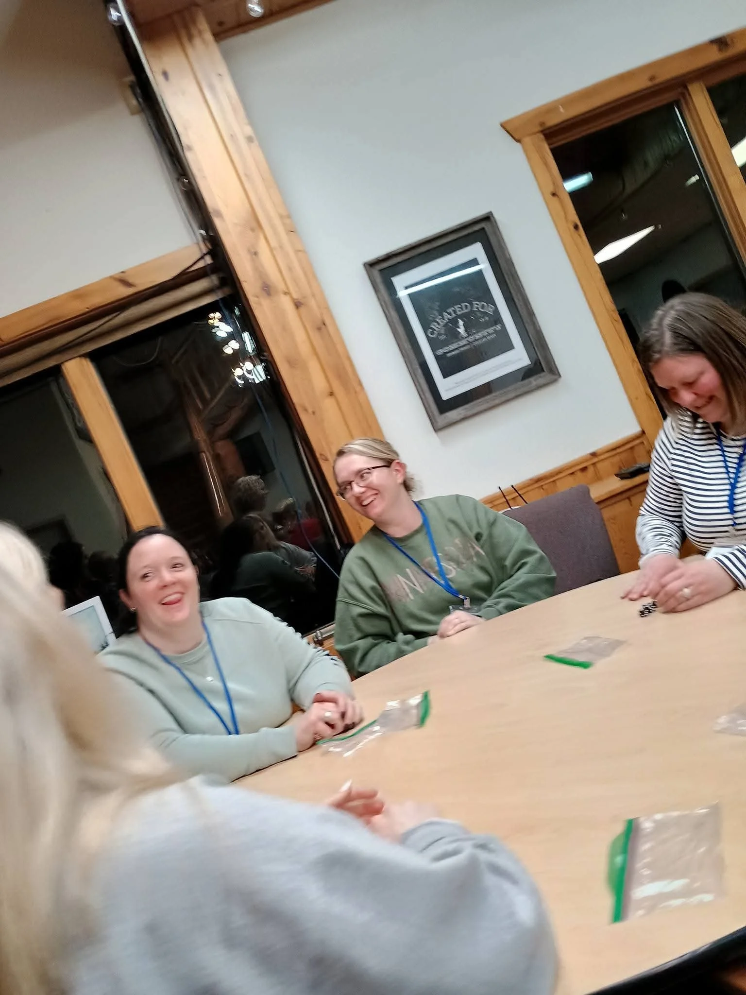 People sitting around a table, smiling and talking, in a cozy room with wooden trim and a framed sign on the wall.
