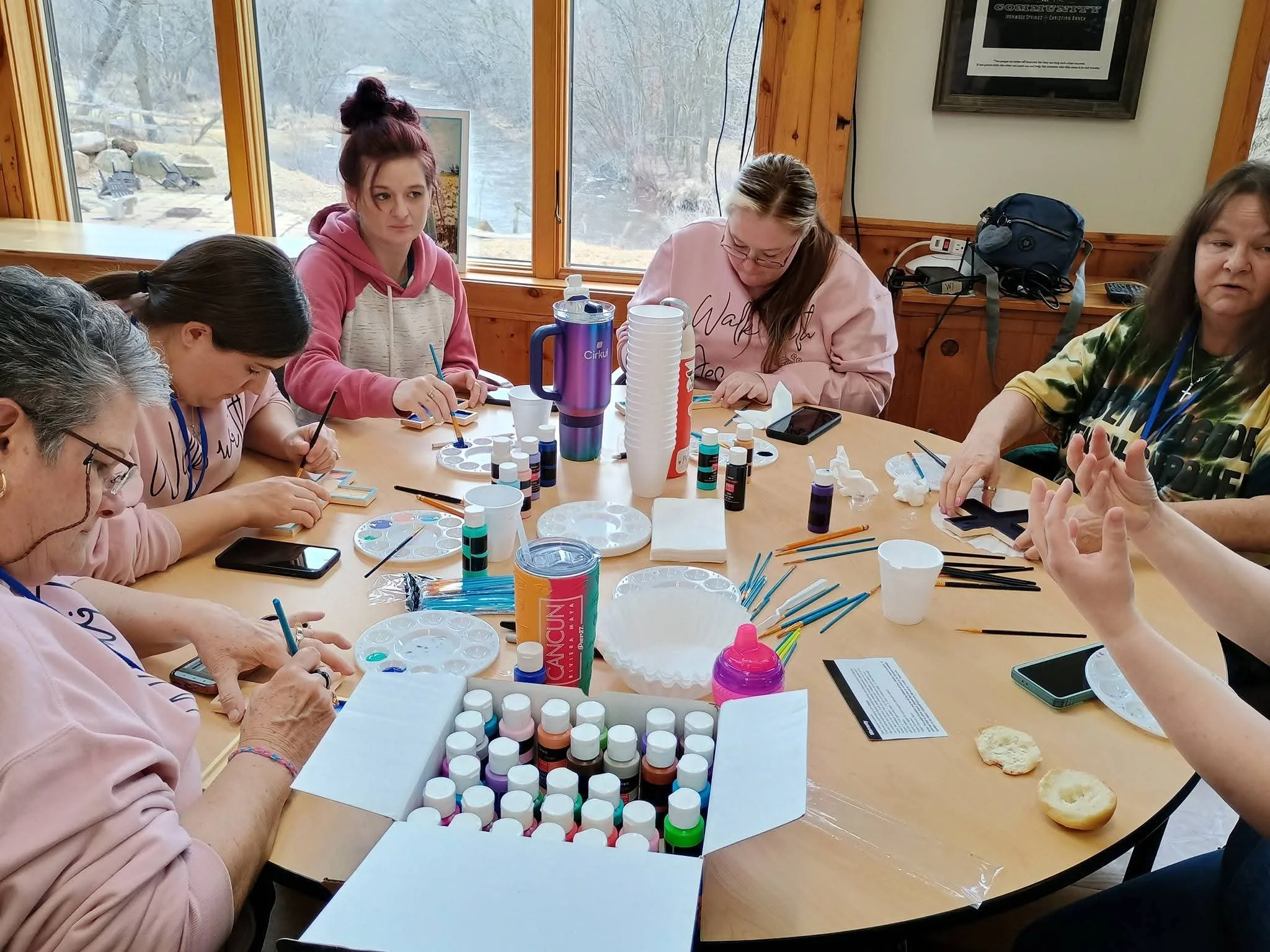 Group of people sitting around a wooden table engaged in nail art activities, with various bottles of nail polish and tools.