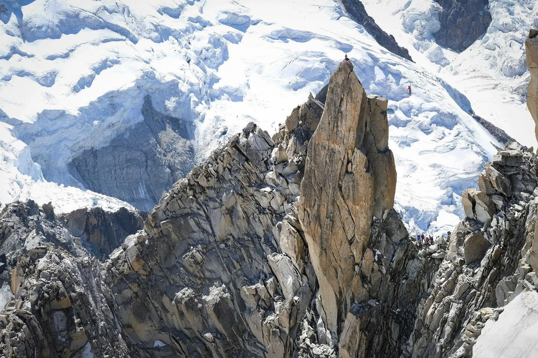 Mountain climbers on a rugged, snow-covered mountain ridge with steep cliffs and icy slopes.