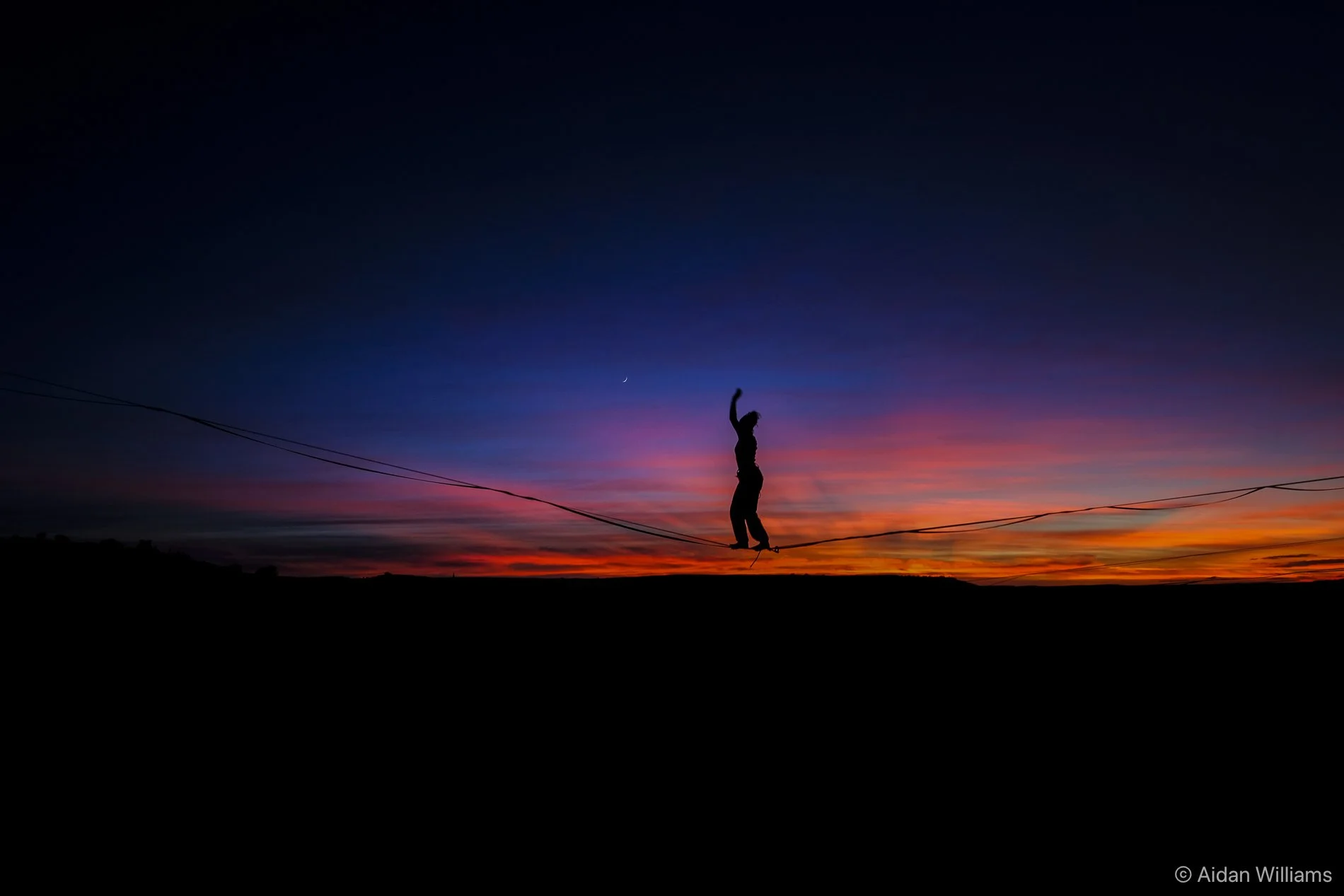 Silhouette of a person walking on a tightrope at sunset with a colorful sky in the background.