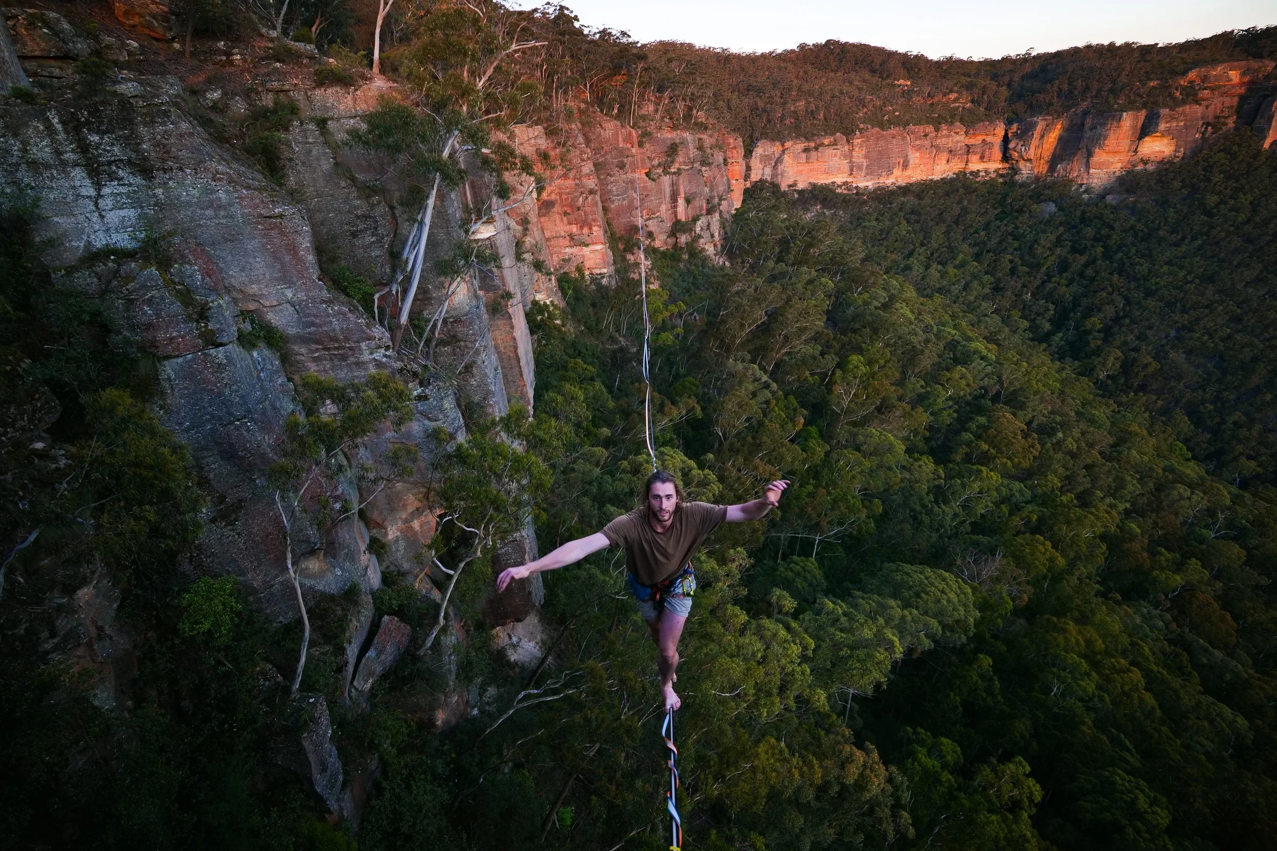 A person is walking a tightrope high above a forested valley.