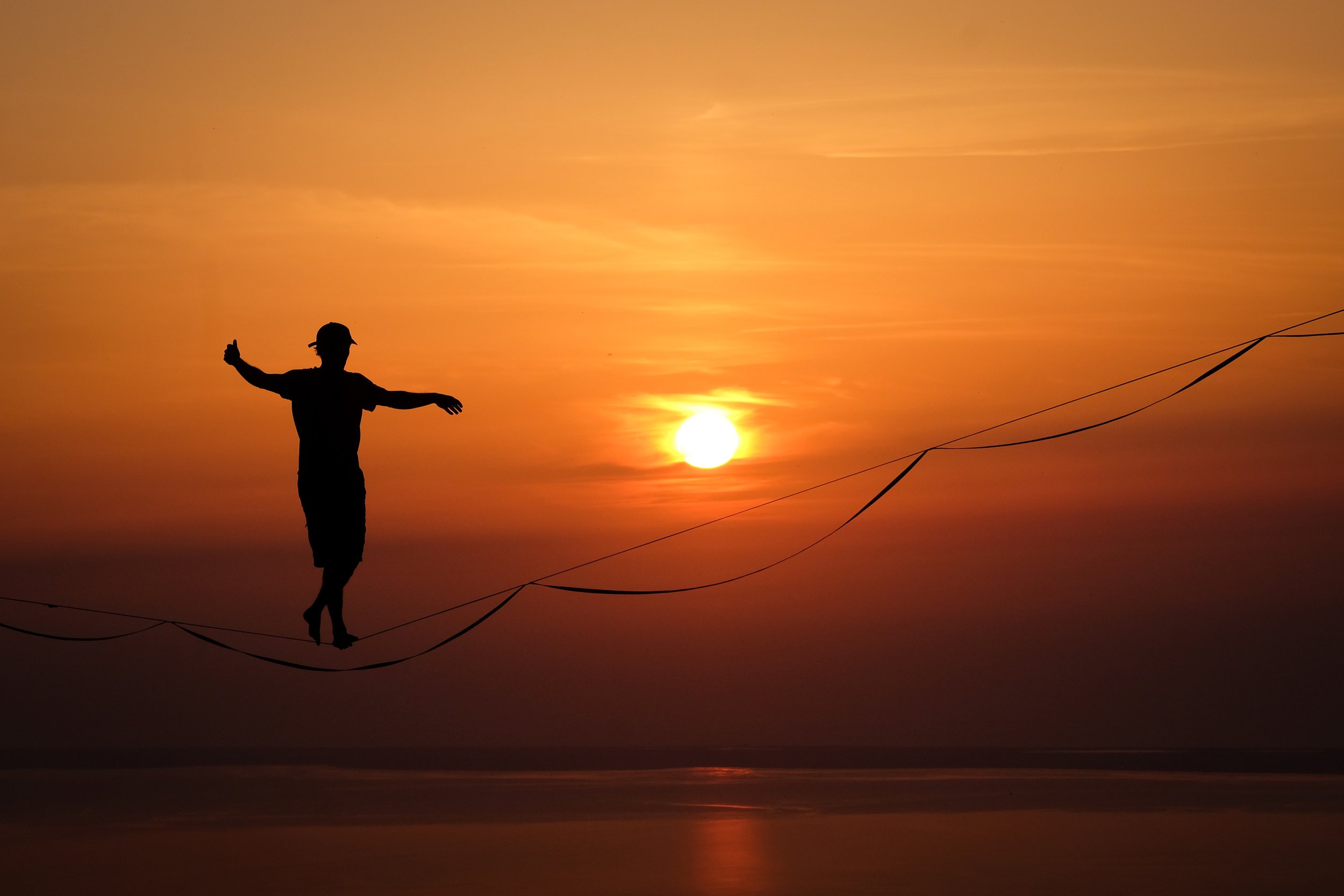 Silhouette of a person walking on a tightrope during sunset over the ocean.