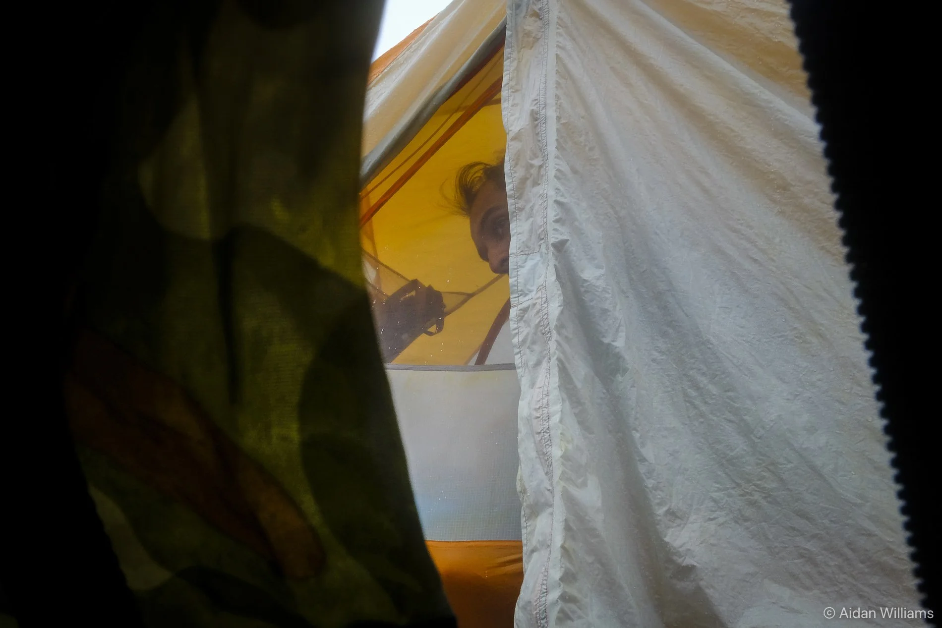 A person is inside a tent, seen through a small opening, with part of the tent's fabric surrounding them.