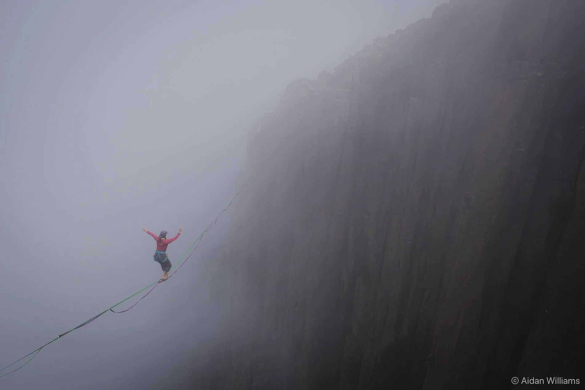 A person balancing on a tightrope stretched across a deep canyon with mist and cliffs in the background.