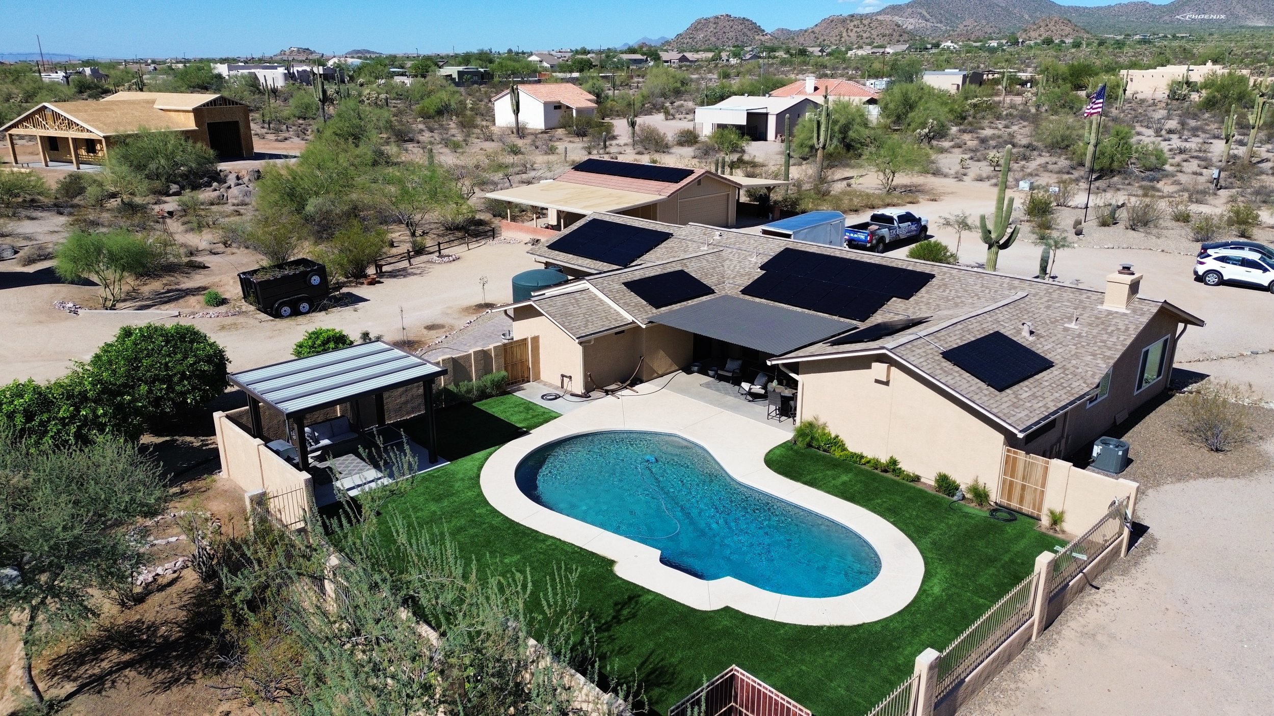 Aerial view of a house with a backyard swimming pool, surrounded by desert landscape, with solar panels on the roof, and cacti in the distance in Arizona