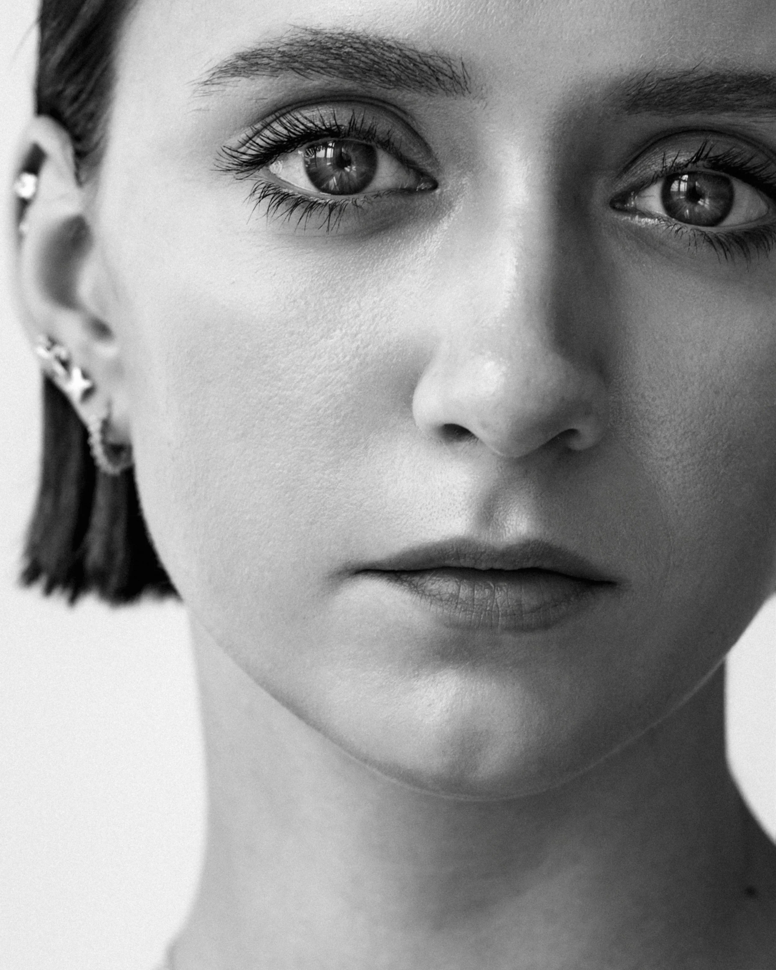 Close-up black and white portrait of a young woman's face, showing her eyes, nose, and lips.