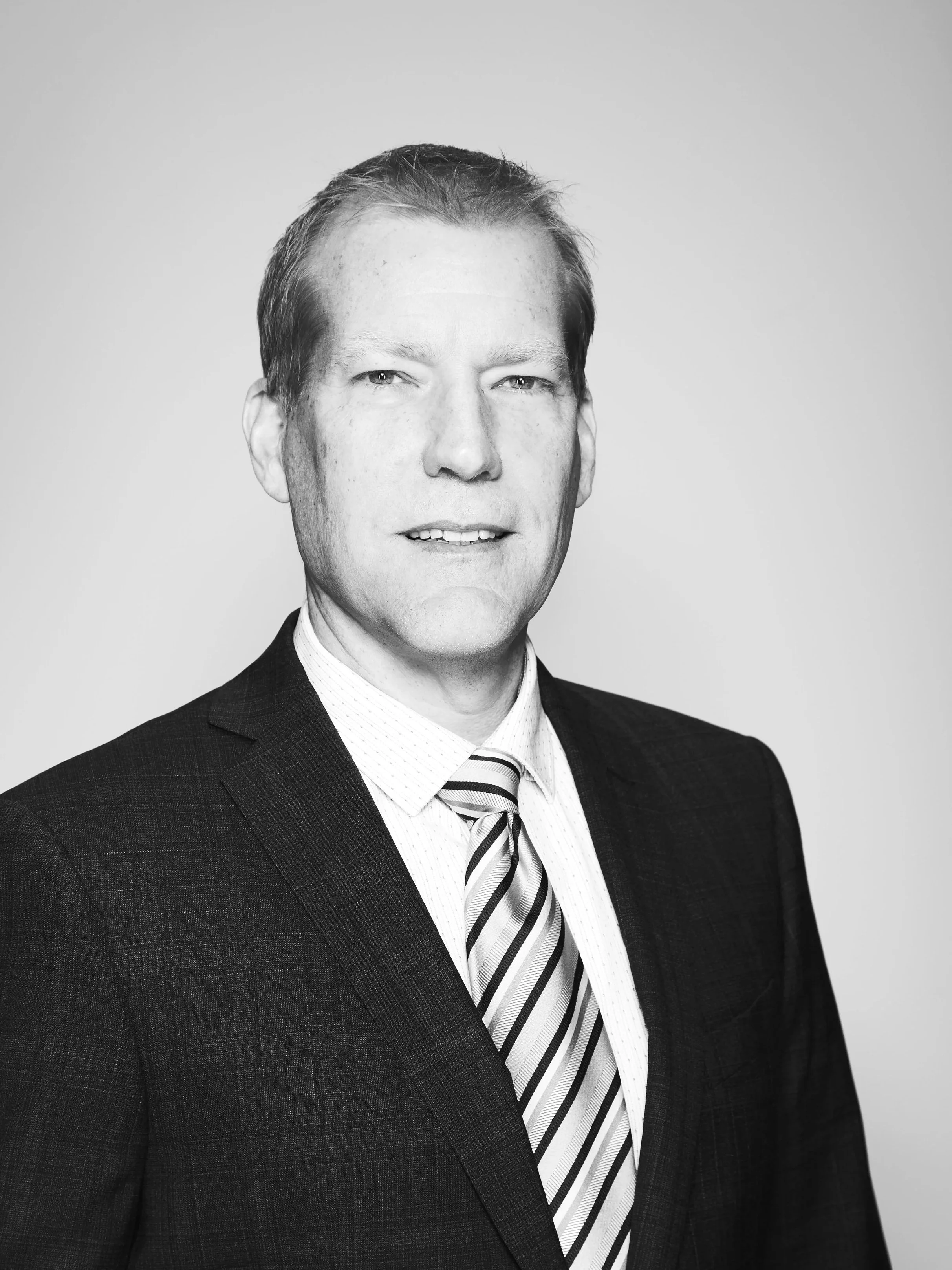 Black and white portrait of a man in a suit and striped tie, looking at the camera against a plain background.