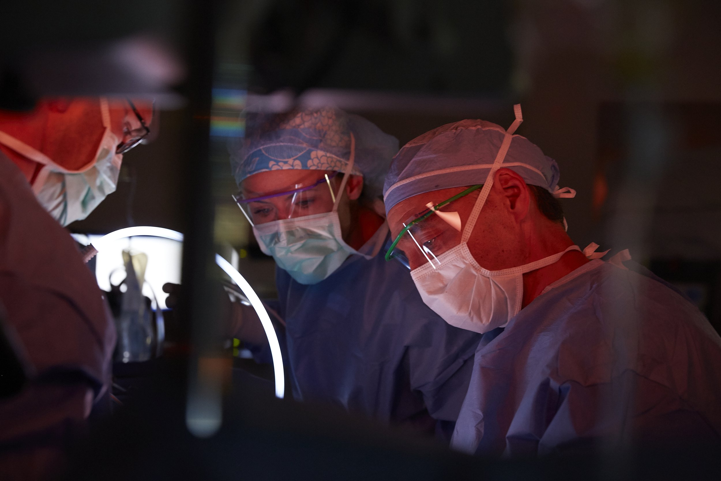 Medical professionals wearing face masks, protective glasses, and surgical caps performing surgery in an operating room.