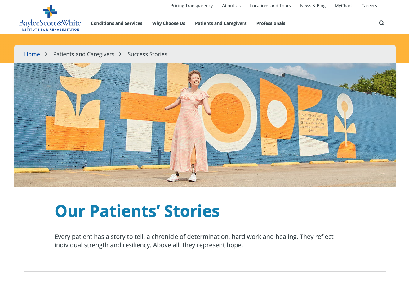 A woman standing in front of a colorful mural painted on a brick wall, smiling and wearing a pink dress and white sneakers.