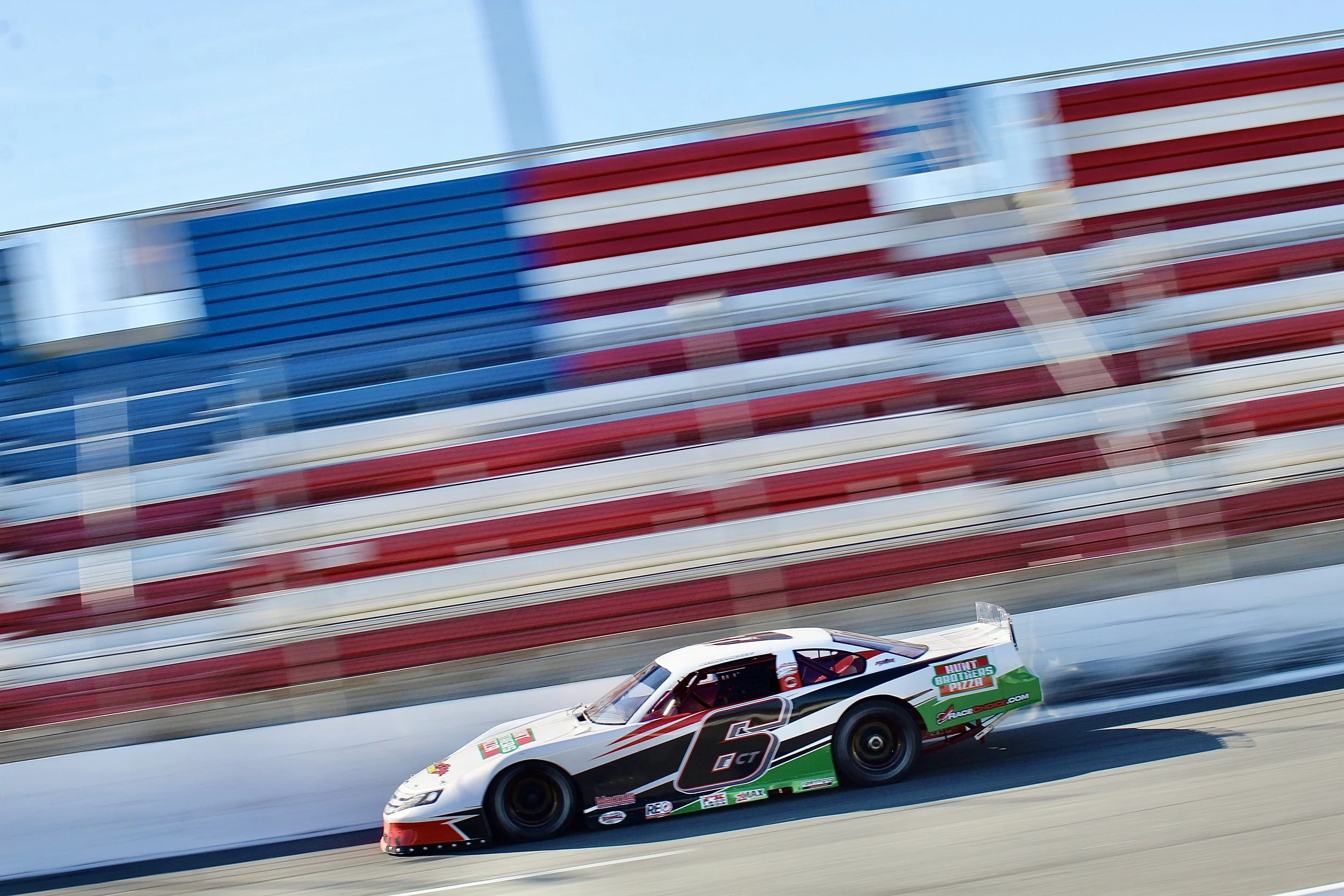 Race car speeding on a racetrack with a blurred American flag in the background.