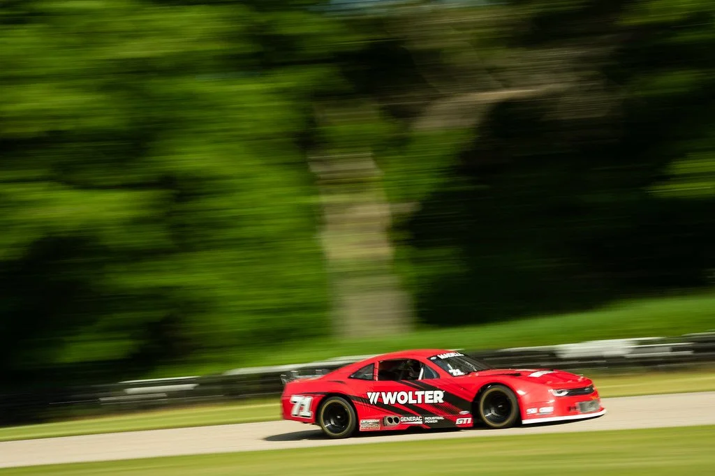 A red race car speeding on a track with a blurred green background.