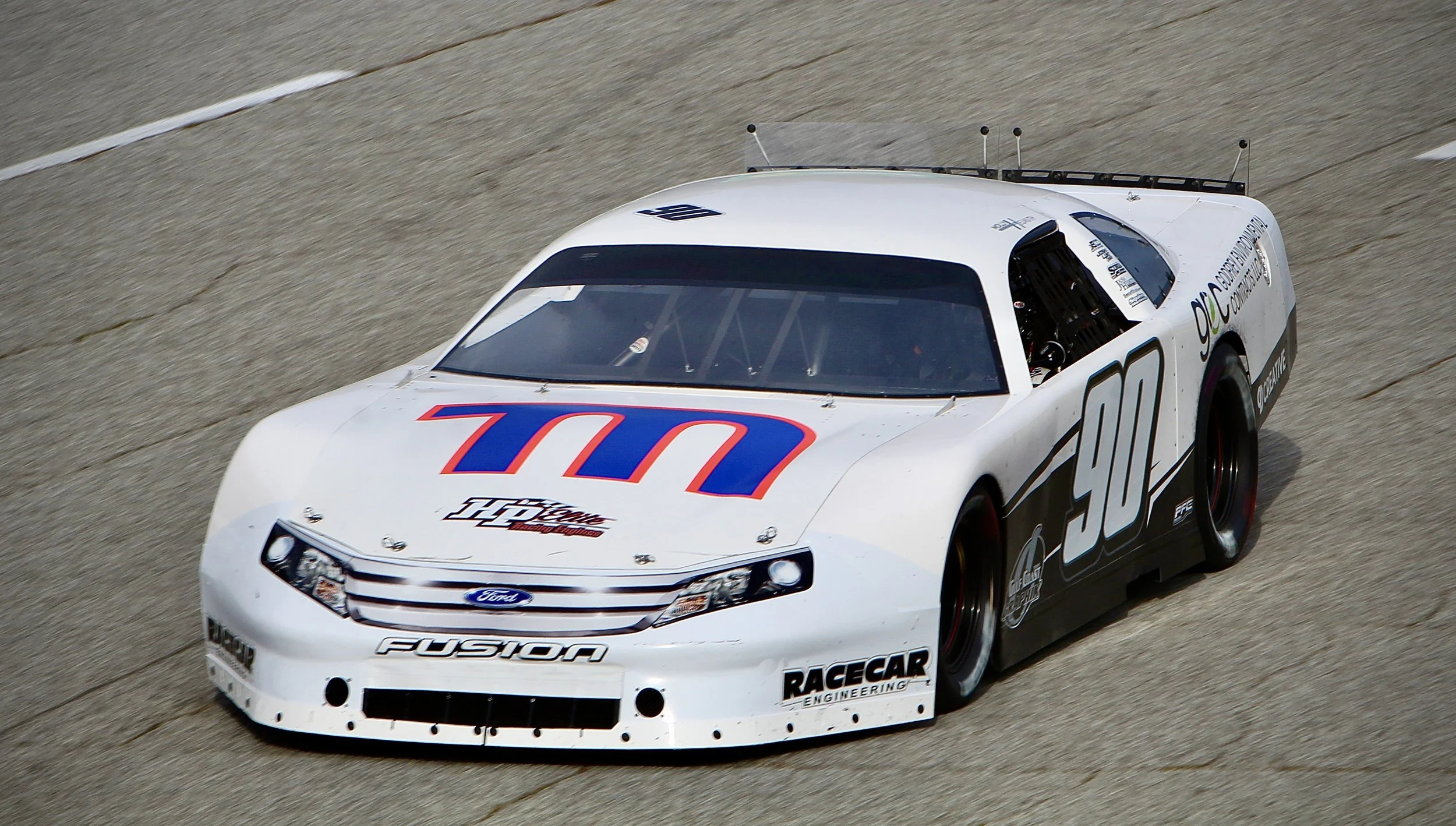 A white race car with the number 90 on its side, racing on a track, featuring logos for Ford, Fusion, Racecar Engineering, and other sponsors.