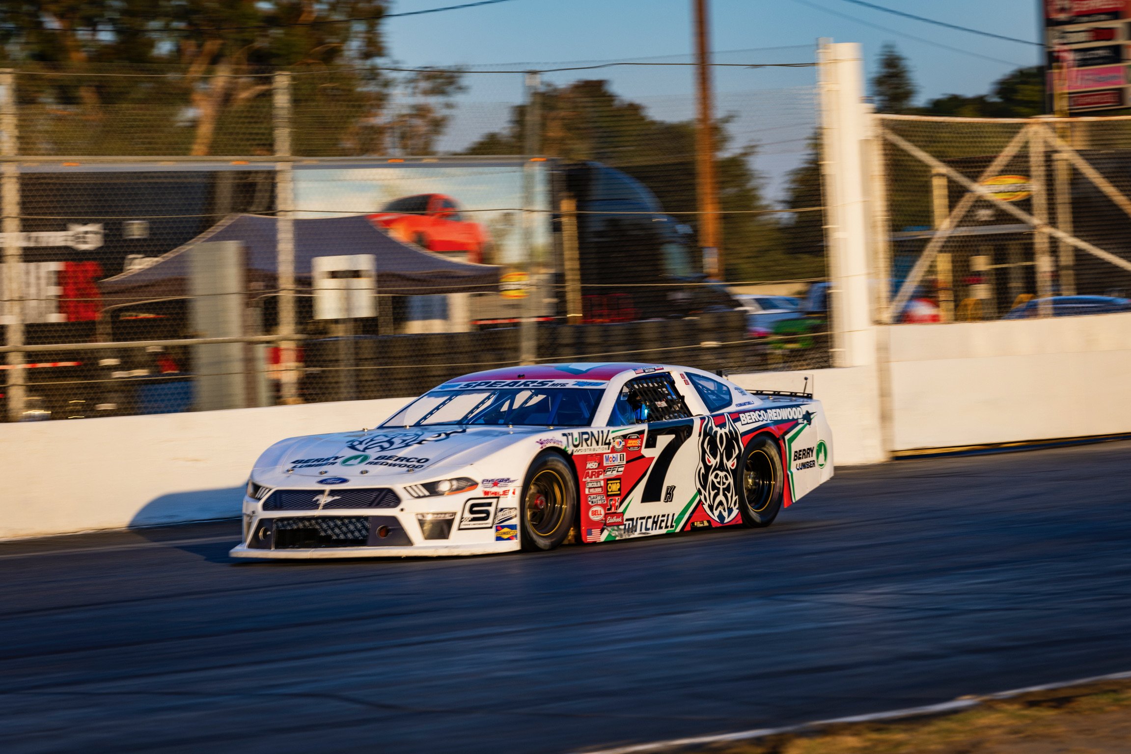 Race car on a racetrack with a white barrier wall, sponsor decals, and a black, red, green, and white paint job.