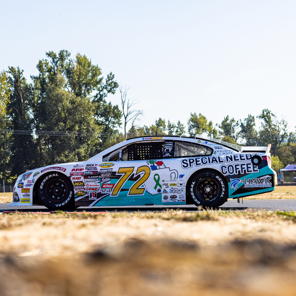 Race car on track with the number 72, sponsor logos, and messages supporting cancer awareness and mental health.