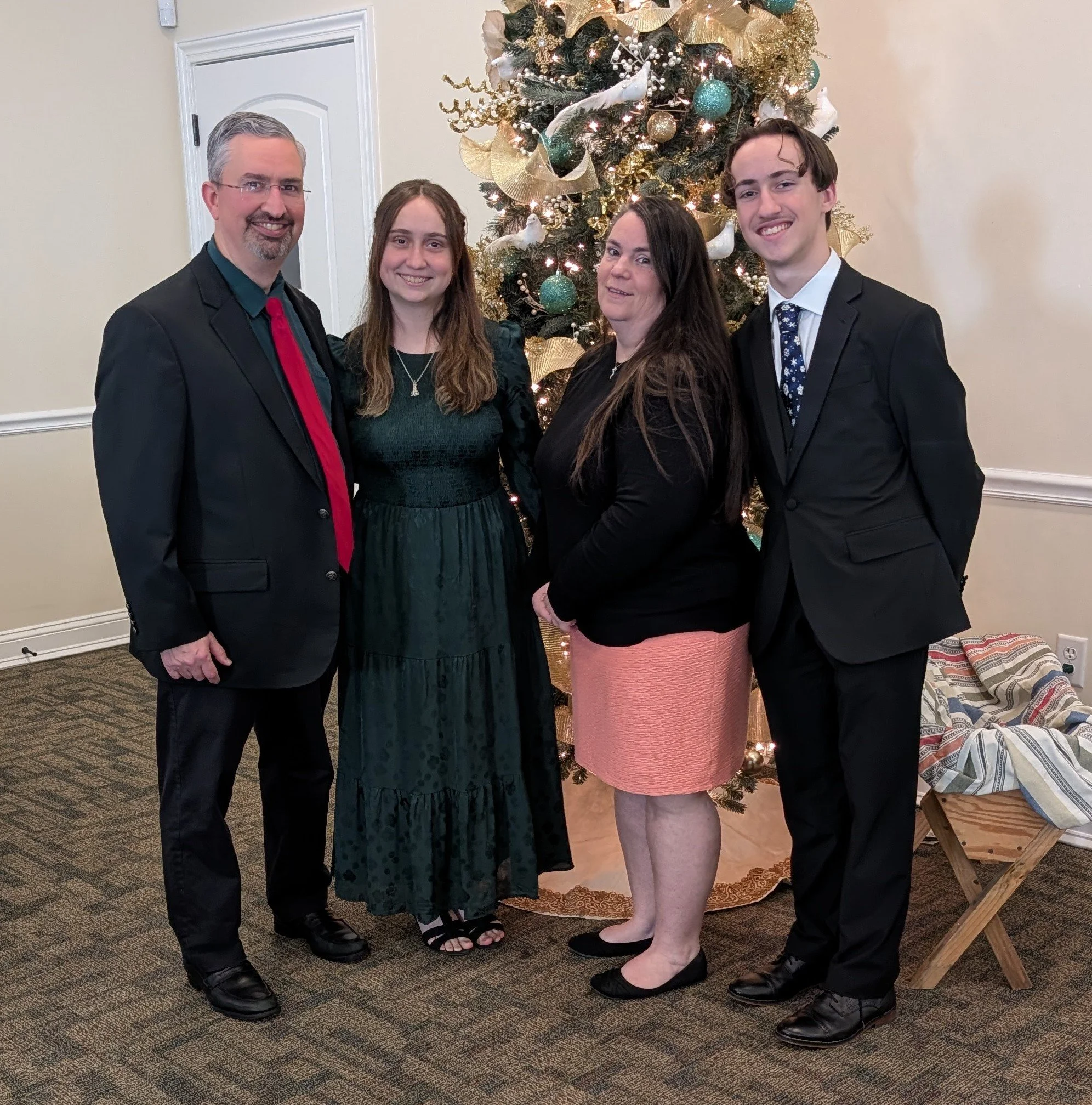 Family of four posing in front of a decorated Christmas tree, dressed in formal winter attire.