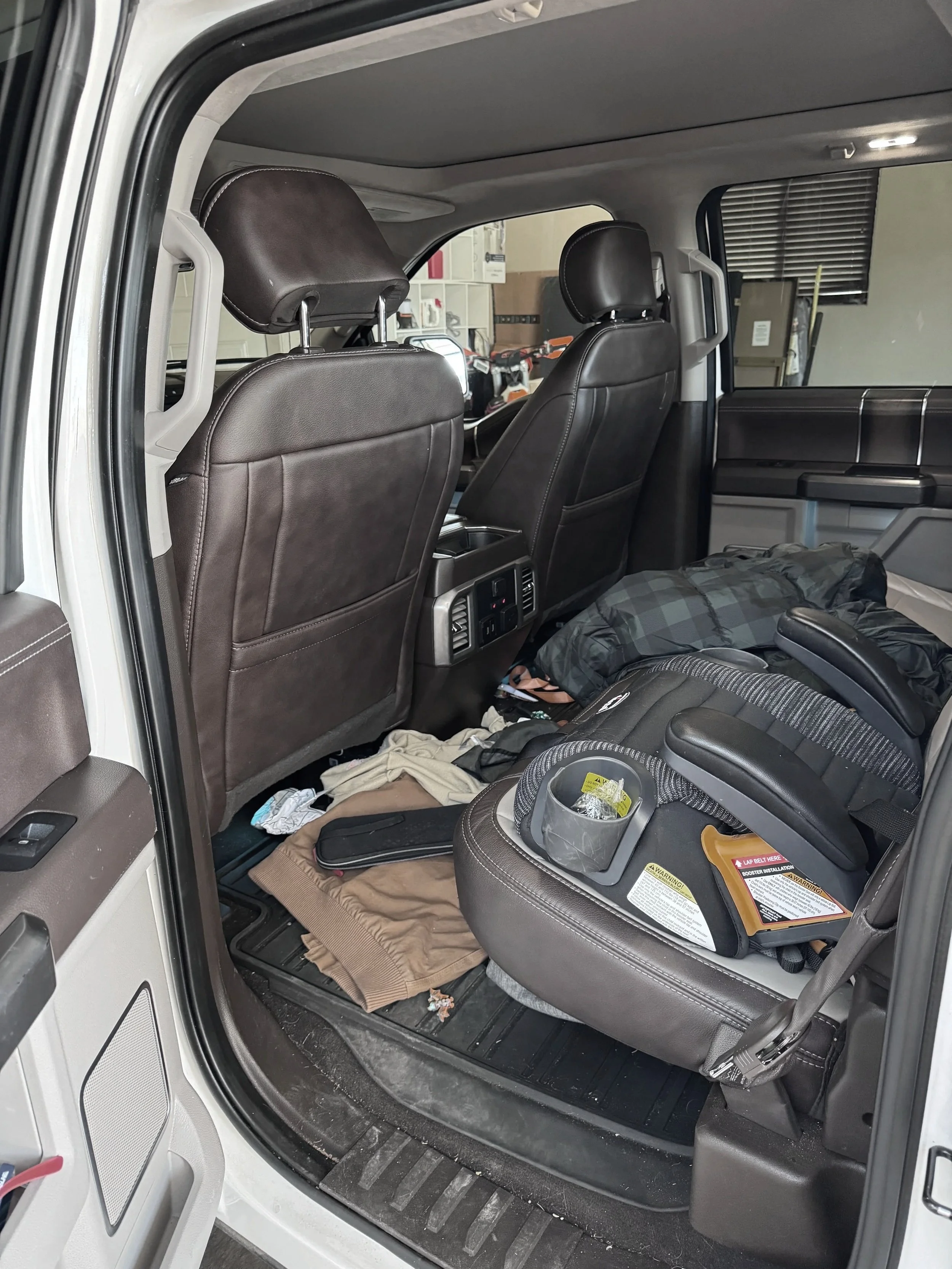 The backseat area of a vehicle with a child car seat, some clothes, and miscellaneous items scattered on the floor.