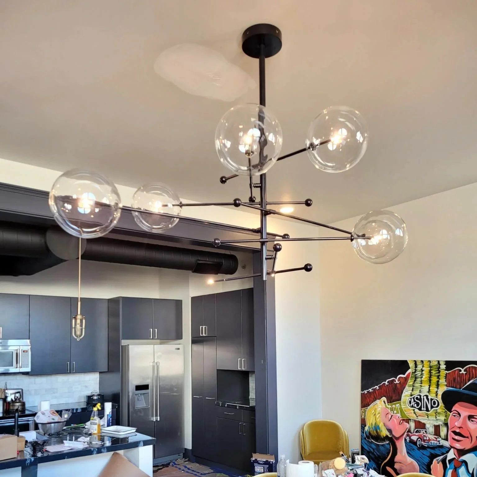 Modern black chandelier with multiple clear glass globes hanging from black rods in a contemporary apartment kitchen.