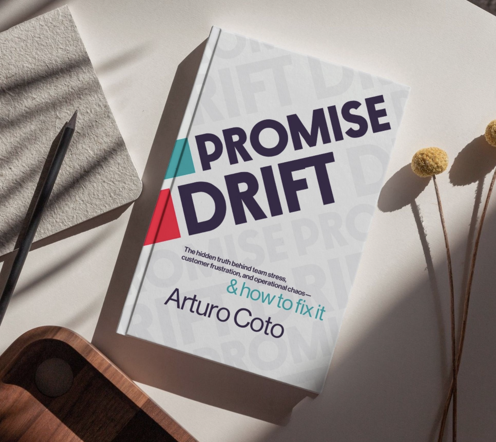 A book titled 'Promise Drift' by Arturo Coto, placed on a white surface with shadow lines. Next to the book are three yellow dandelions with long stems, a piece of textured gray paper, a black pencil, and a wooden object partially visible.
