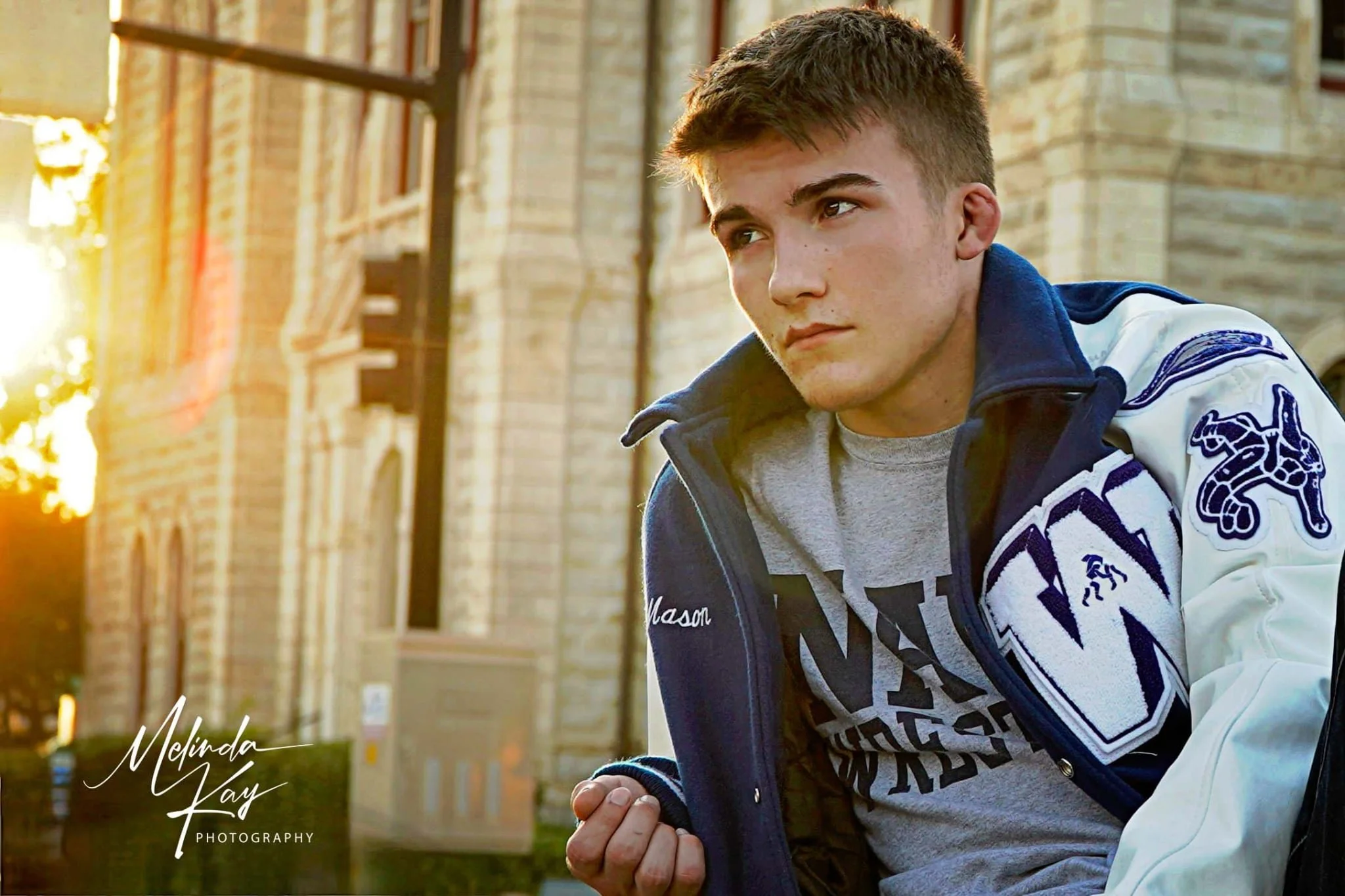 Young man sitting outdoors near a brick building during sunset.