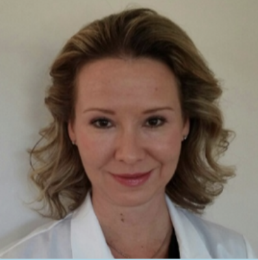 A woman with light brown, wavy hair wearing a white top, smiling lightly at the camera.