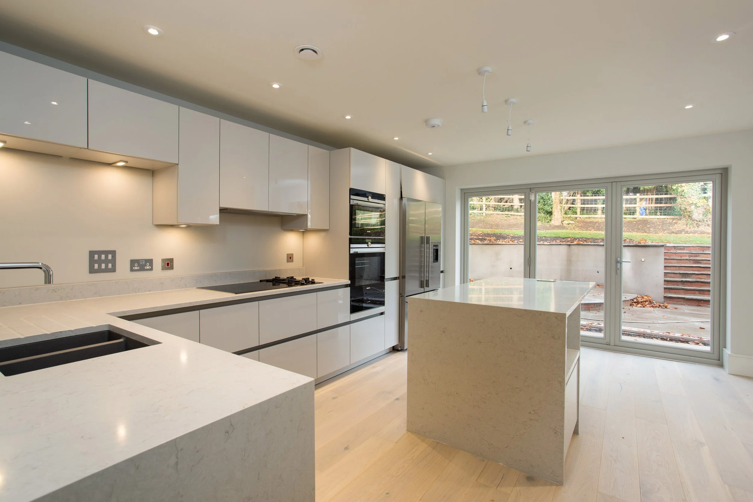 Modern kitchen with white cabinets and countertops, stainless steel appliances, a large sliding glass door leading to an outdoor area, and an island in the center.