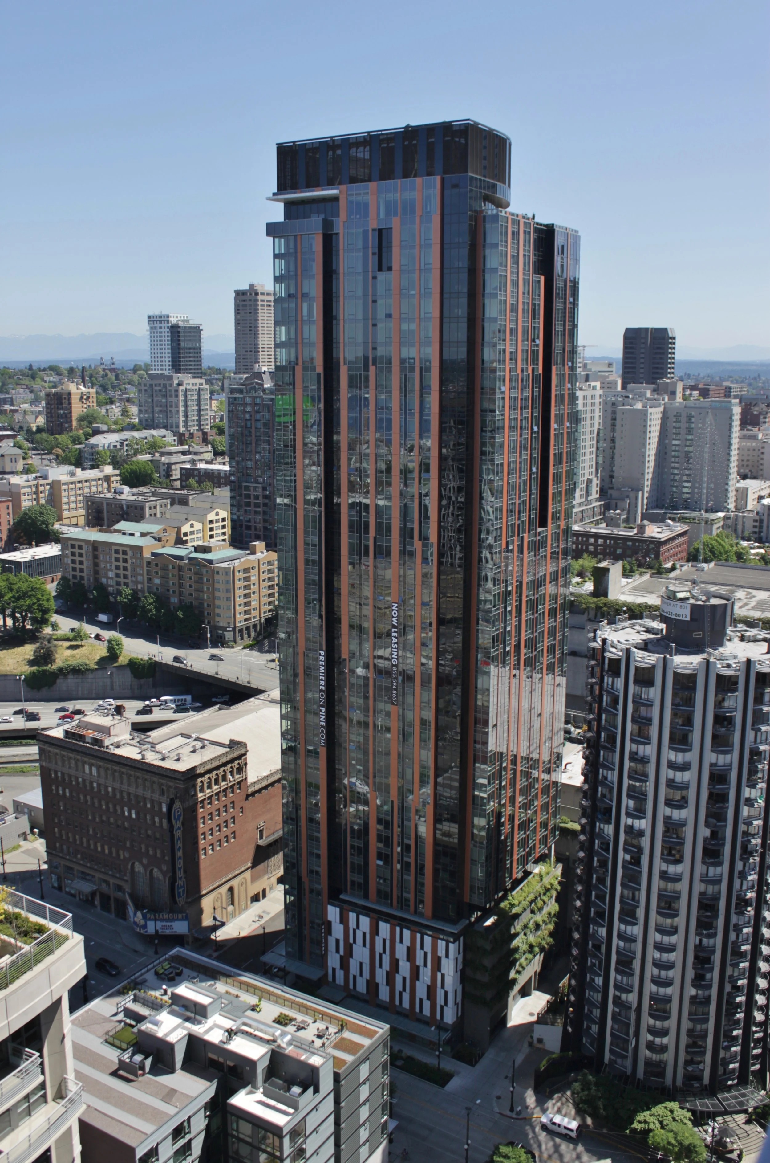 Tall modern glass skyscraper with a dark top, located in an urban cityscape with various other buildings and streets visible.