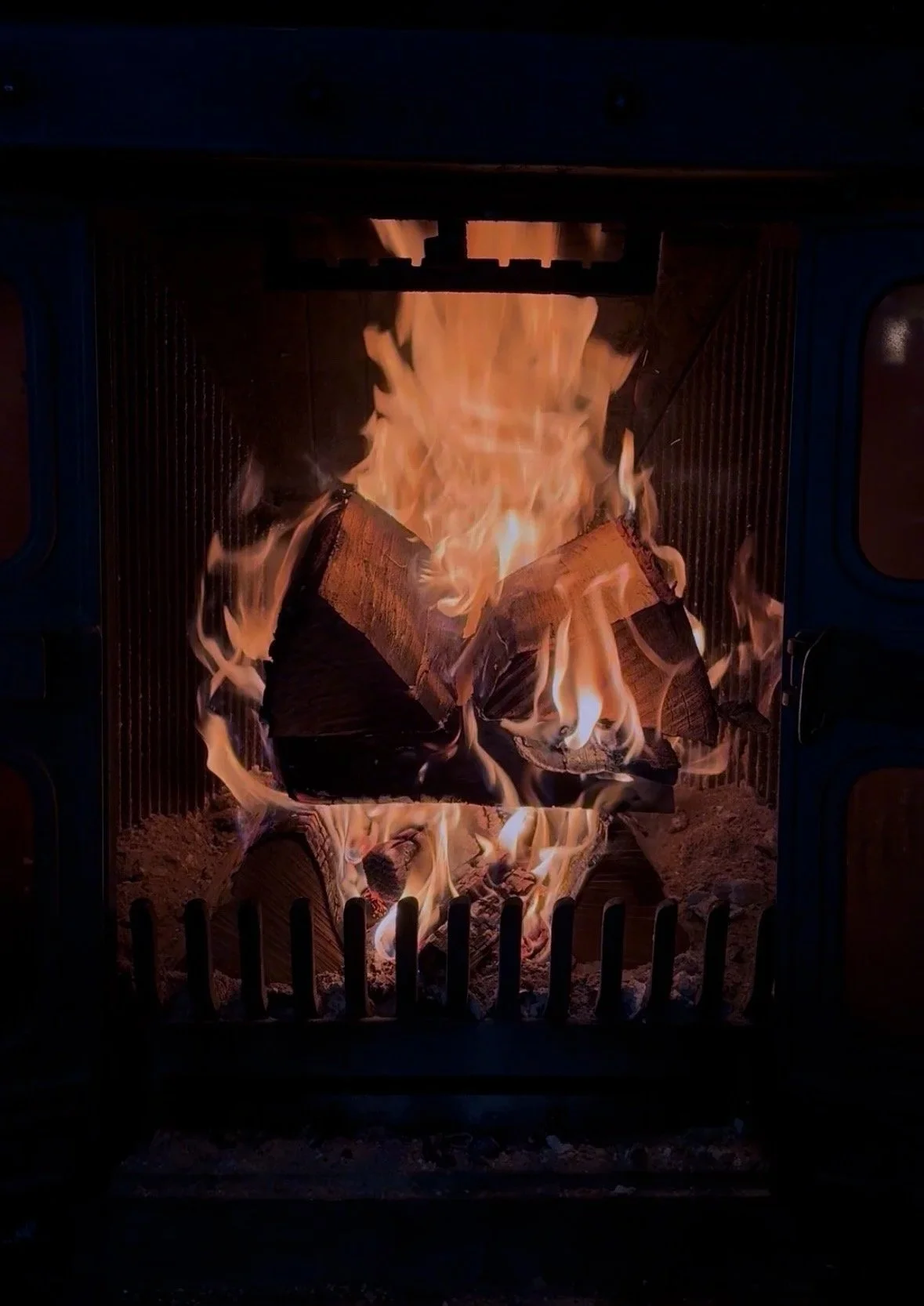 Fire burning inside a metal grill or fireplace, with wood logs on fire.
