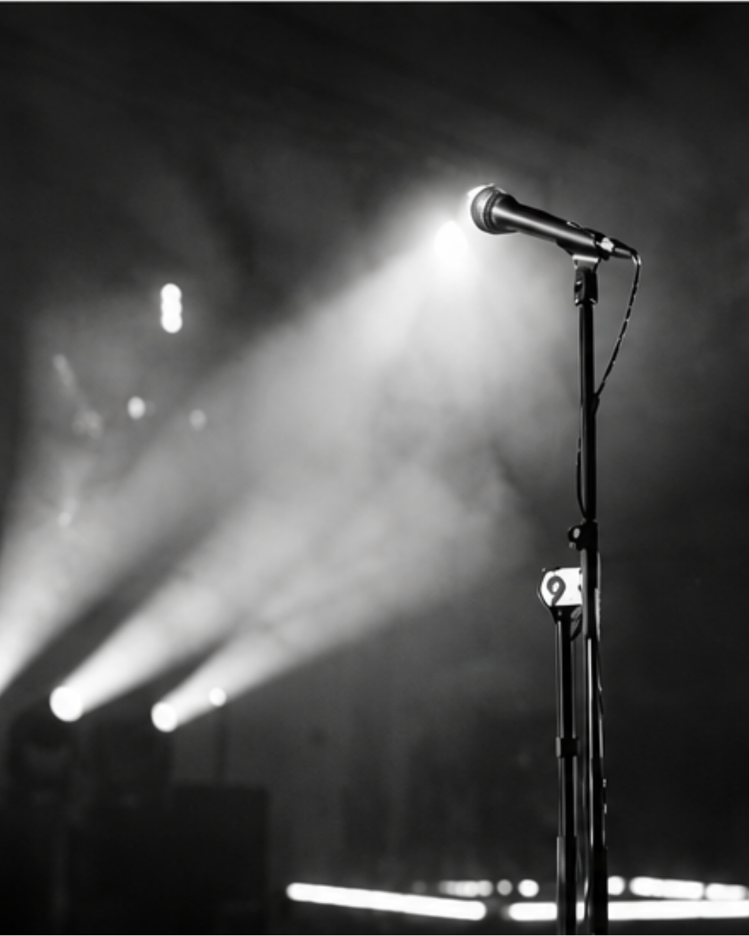 Microphone on an empty stage beneath bright performance lights.