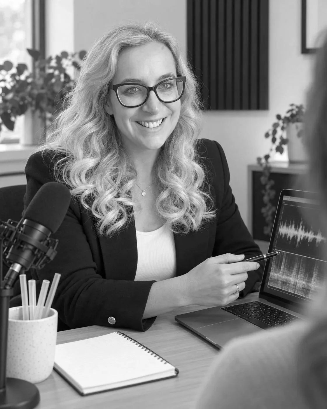 Amy Oughton smiling at a desk with a notebook, laptop and microphone.