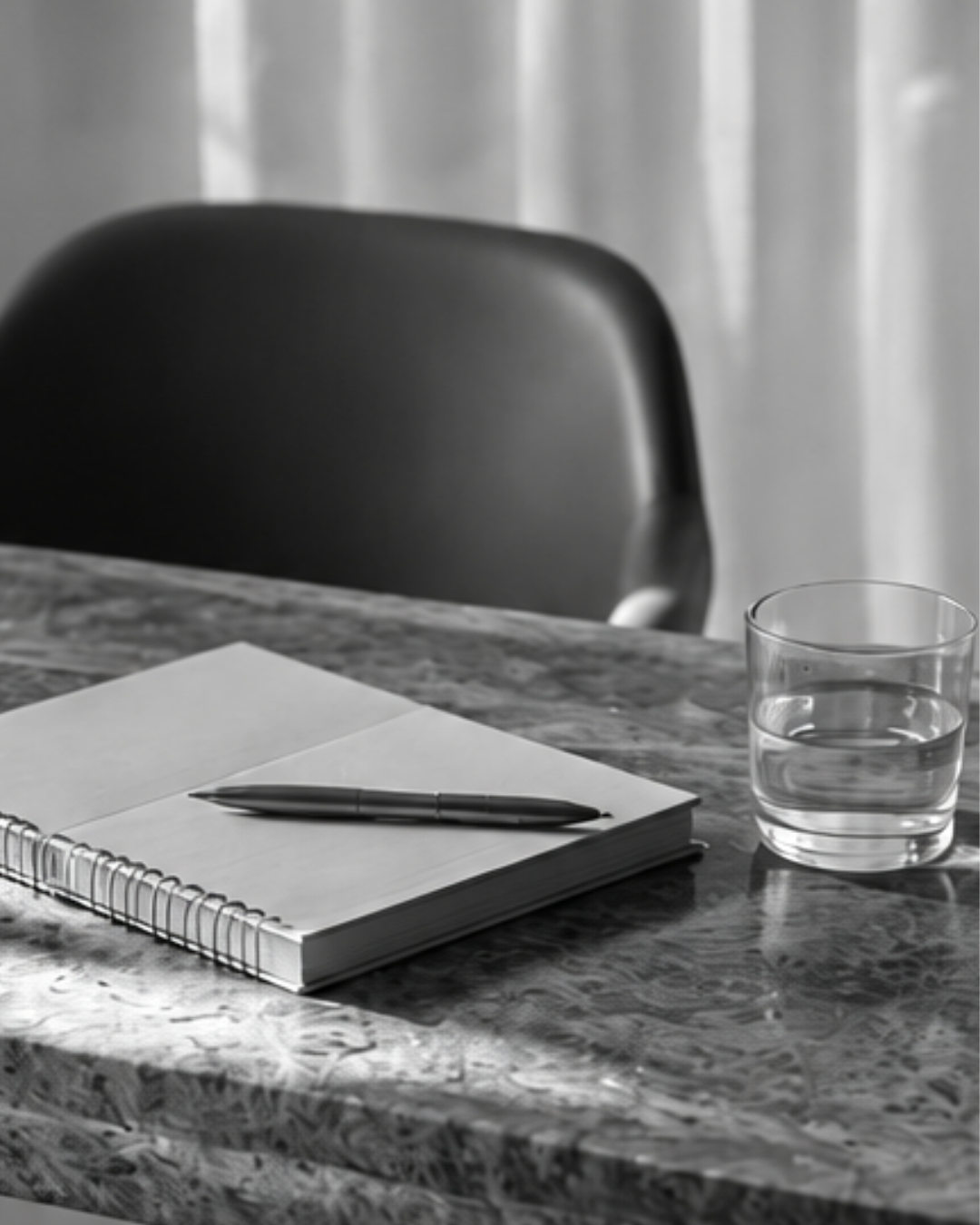 Notebook, pen and glass of water arranged on a marble table.