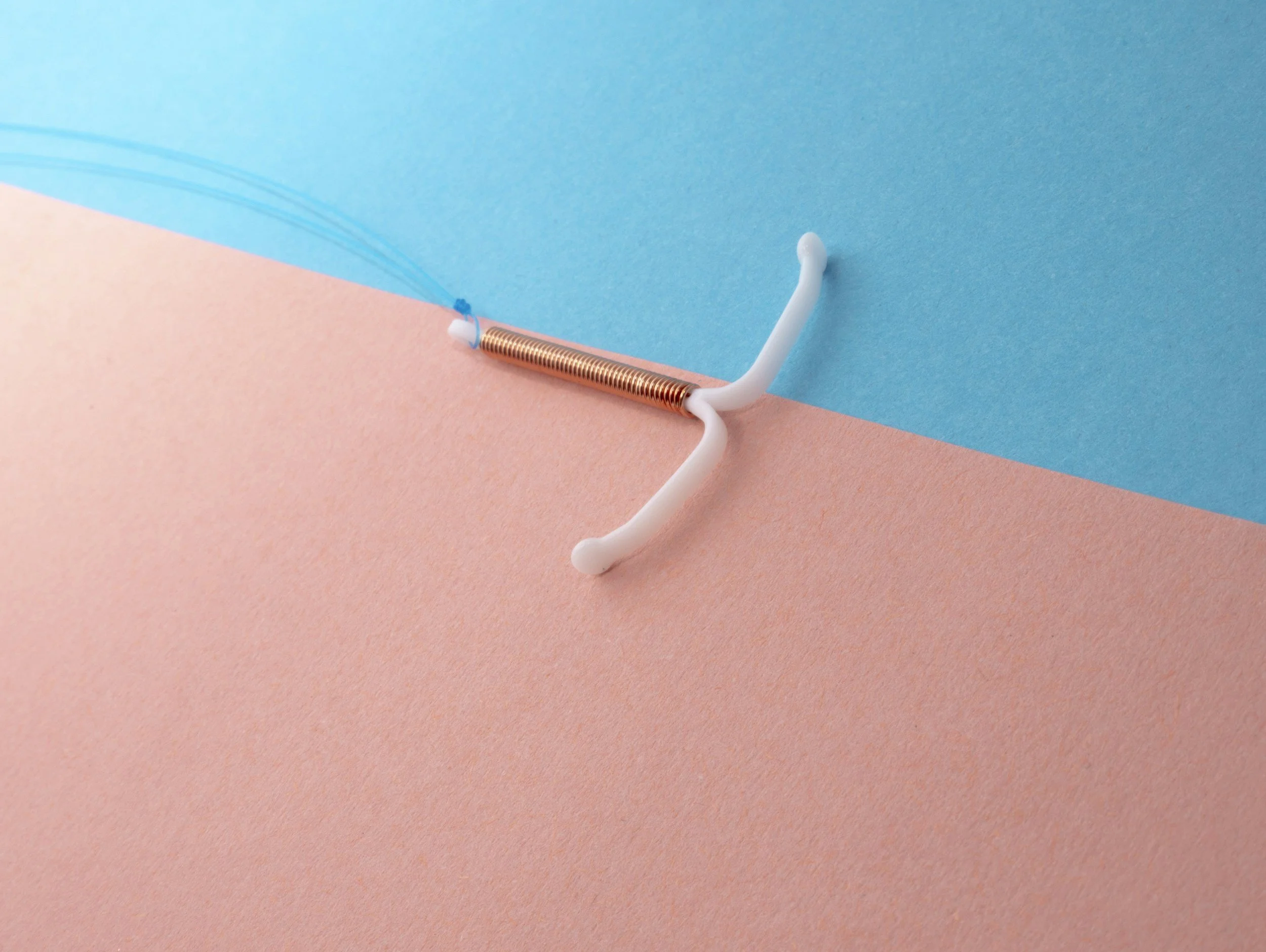 A colorful background with pink and blue textured paper, featuring a plastic and metal spring toy with some strings attached.