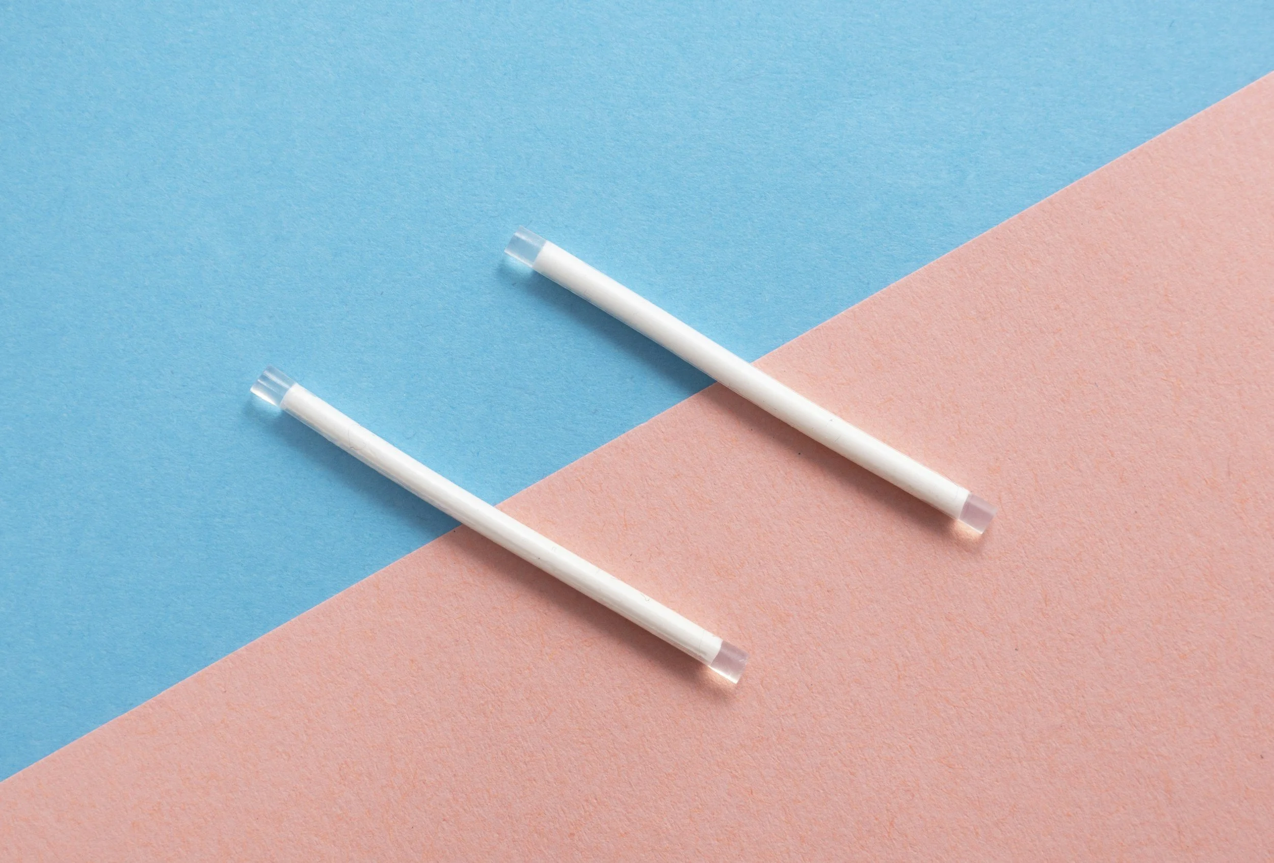 Two white disposable vape pens placed diagonally on top of blue and pink textured paper background.