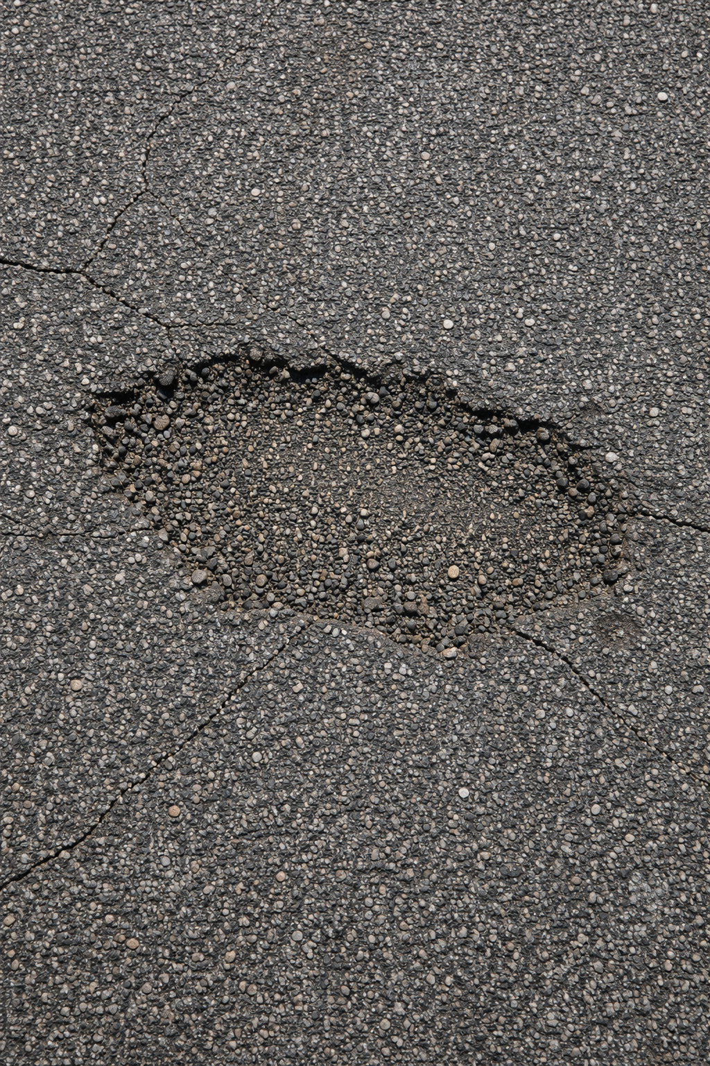 Asphalt pavement surface detail with worn patch outline.