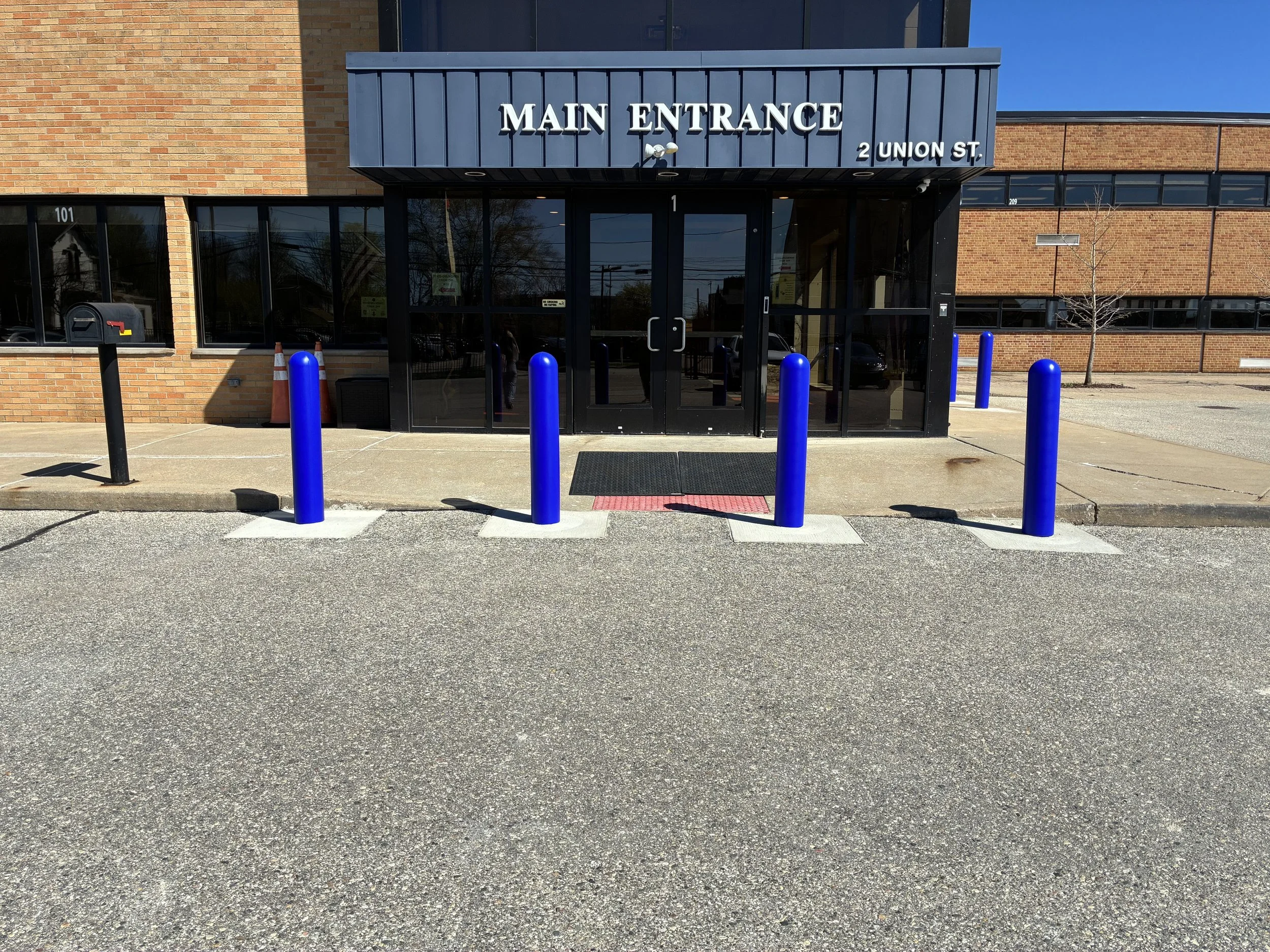 Four crash-rated security bollards with blue decorative covers protecting main entrance at St. Mary Catholic School, 2 Union Street Mount Clemens Michigan, NSGP-funded installation by Trident Industrial Systems