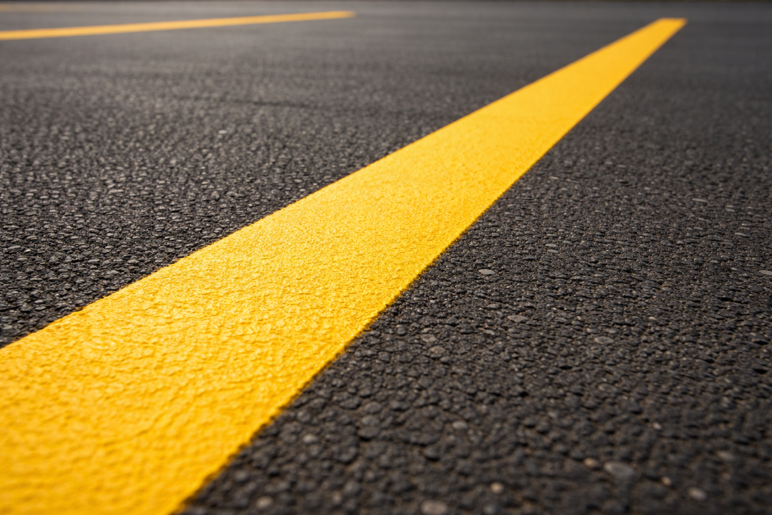 Fresh yellow parking lot striping line on asphalt pavement.