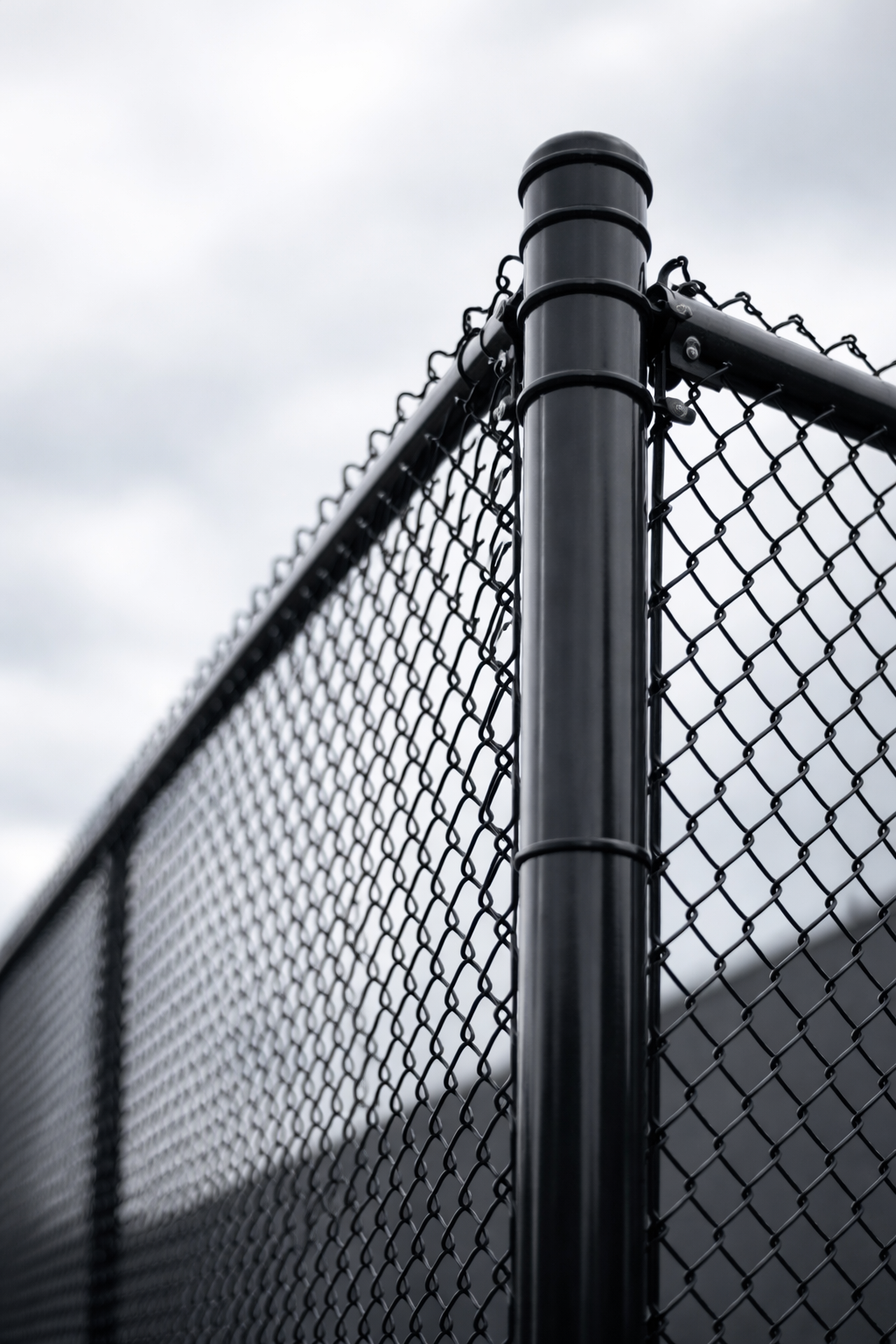 Close-up of a black metal chain-link fence against an overcast sky.