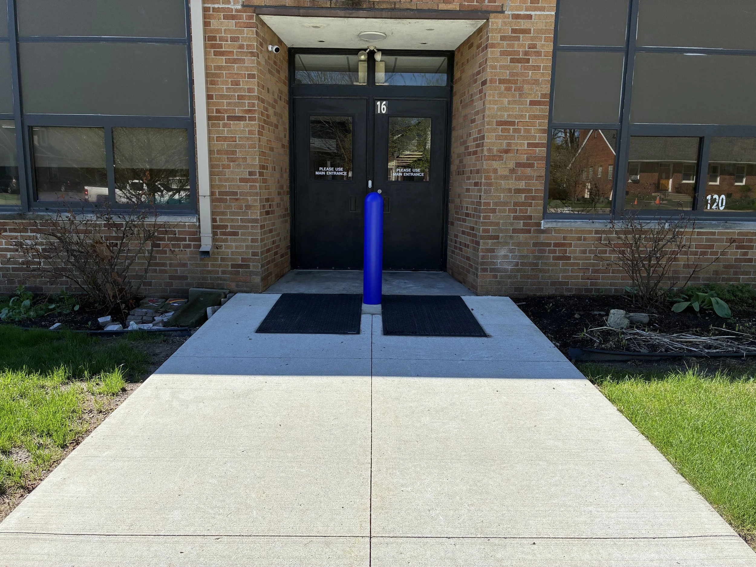 Single blue ASTM C40 crash-rated security bollard with decorative cover protecting rear entrance door 16 at St. Mary Catholic School, nonprofit security grant installation Metro Detroit