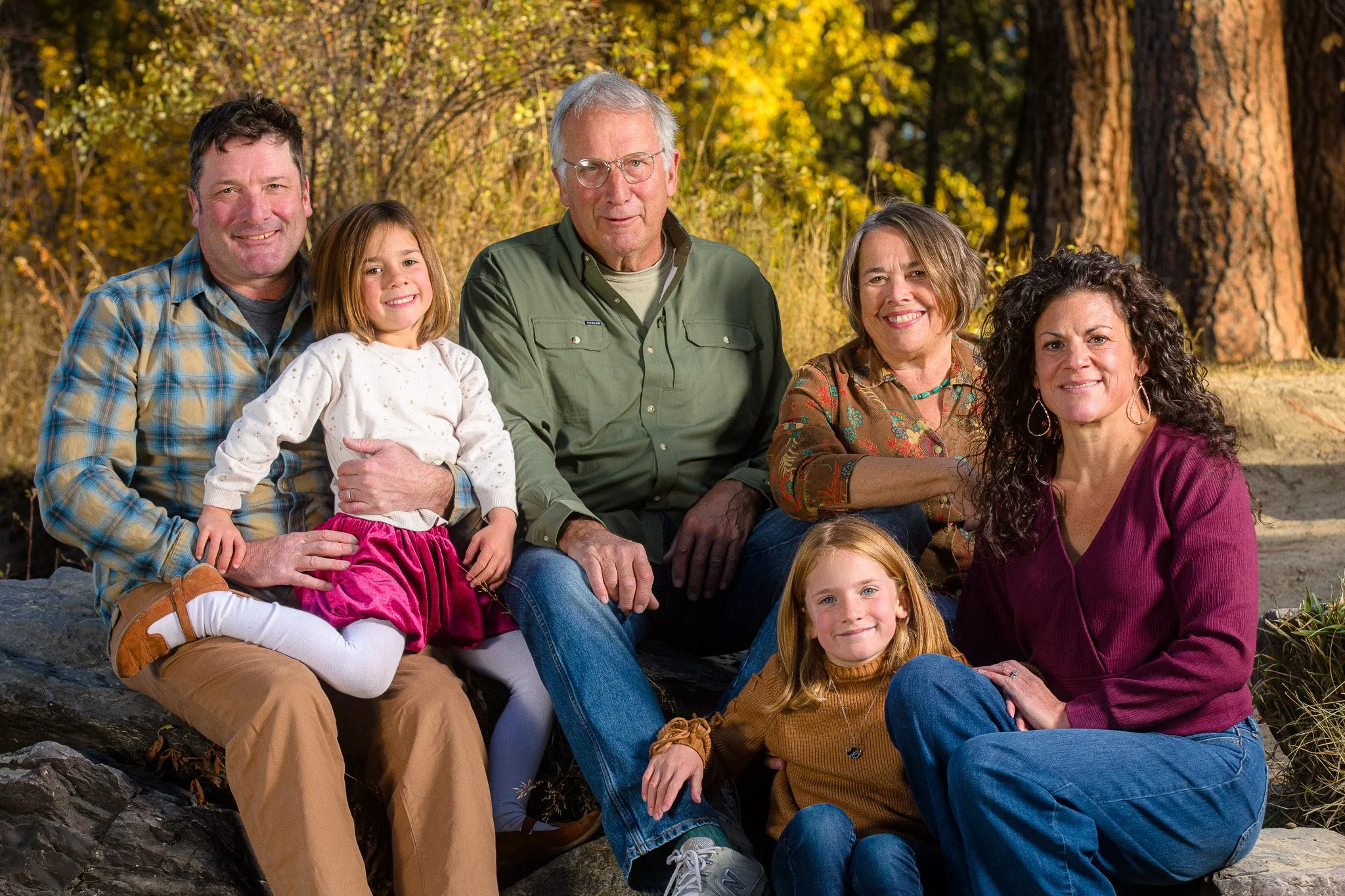 Group of seven family members sitting outdoors in a forested area during autumn.