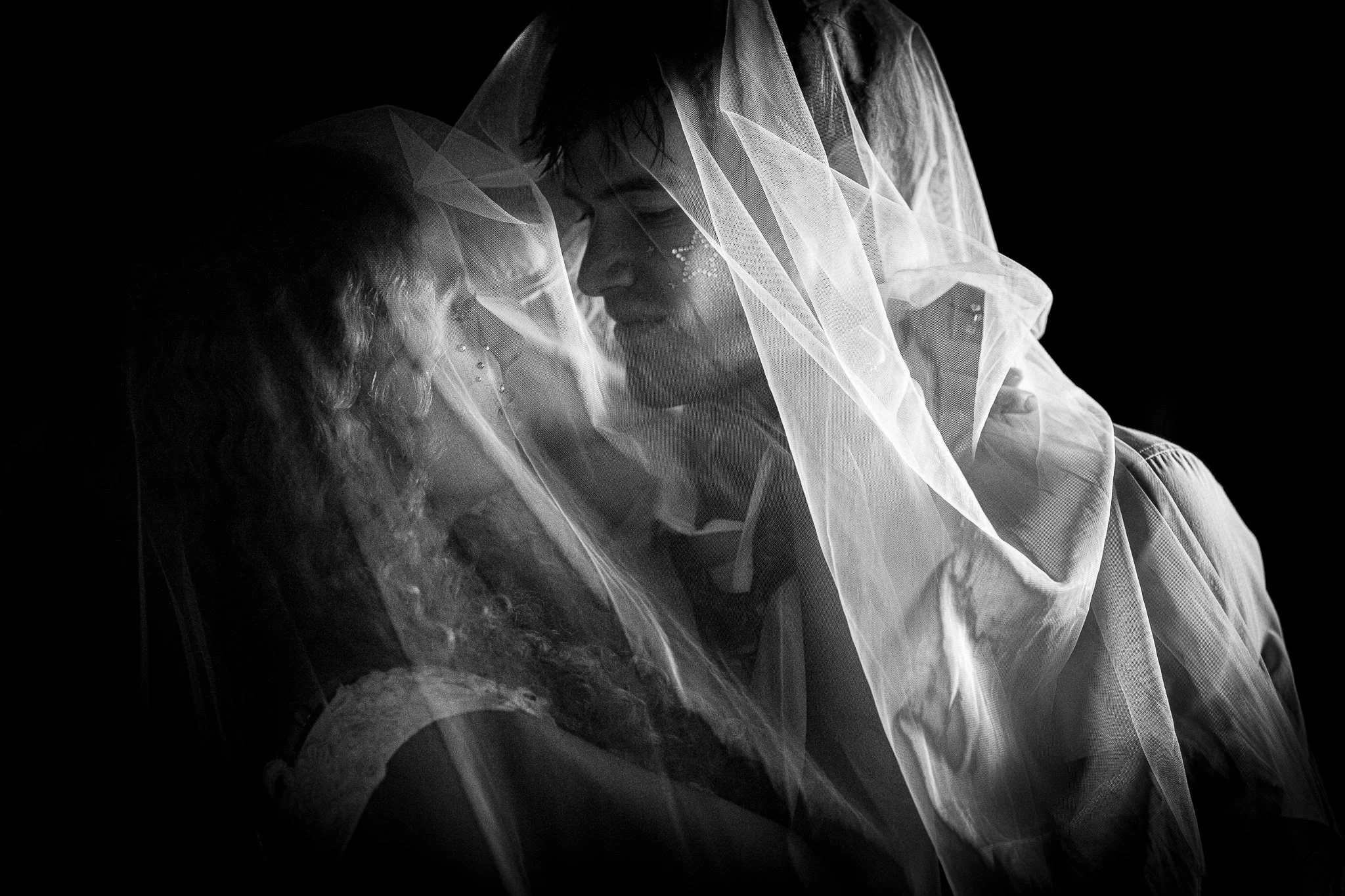 A couple in a close, intimate pose, with a veil draped over their heads, in black and white.