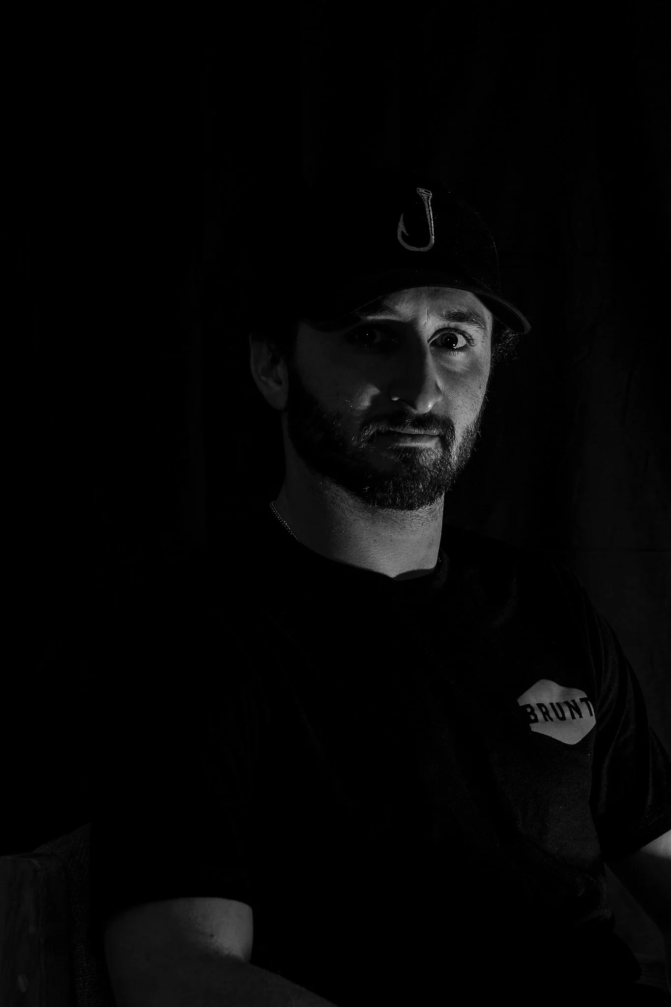 Black and white portrait of a man wearing a cap and t-shirt with a logo.