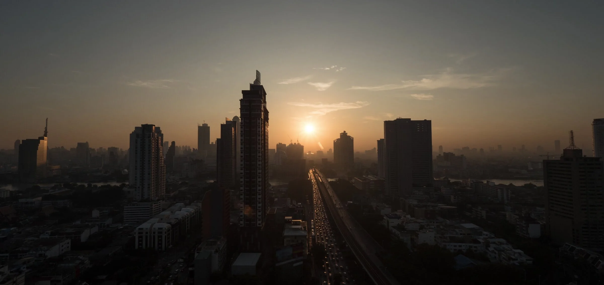 Sunset over a city skyline with tall buildings and a busy highway.