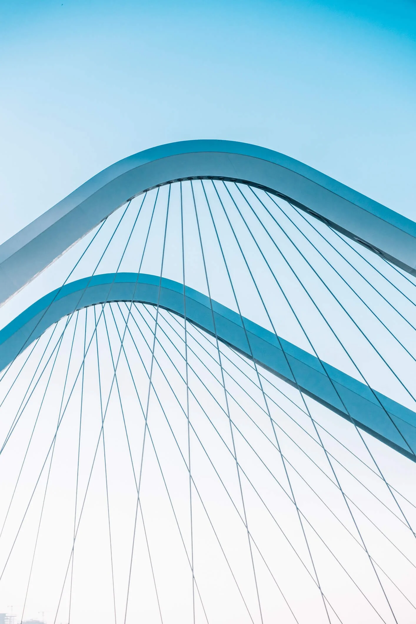 Close-up view of a modern, architecturally unique bridge with curved arches and cable supports against a clear sky.