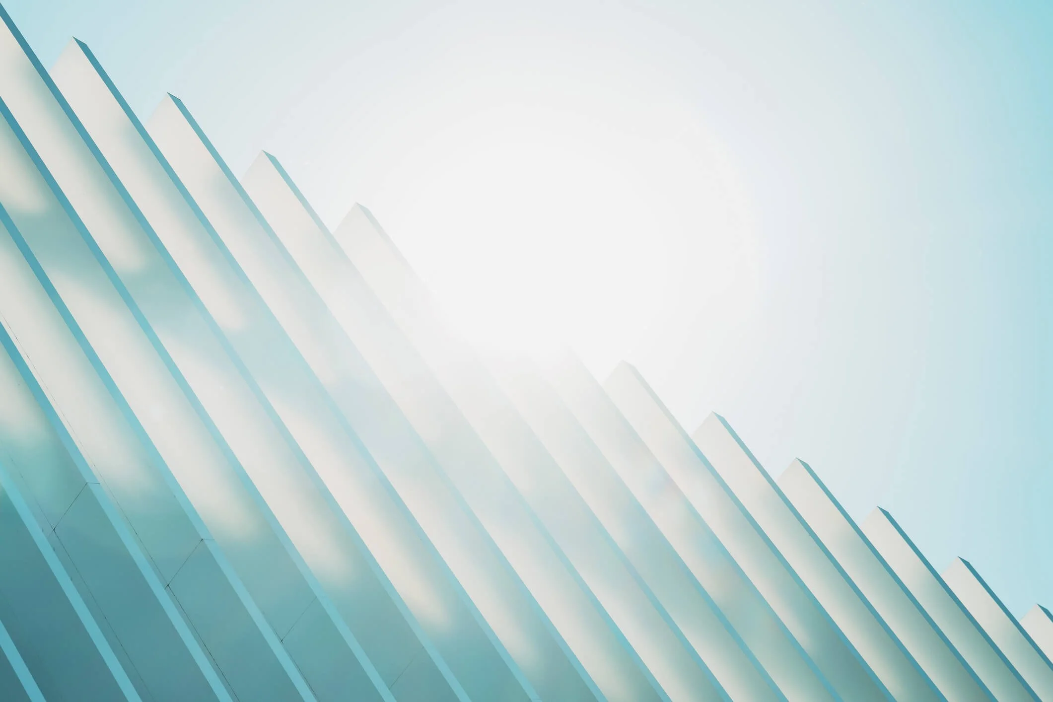 Modern building with blue glass windows and white ledge. The sun is shining brightly in the sky.