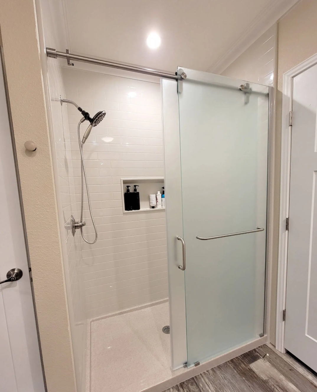 Bathroom shower with frosted glass sliding door, showerhead, built-in shelf with toiletries, and tiled walls.