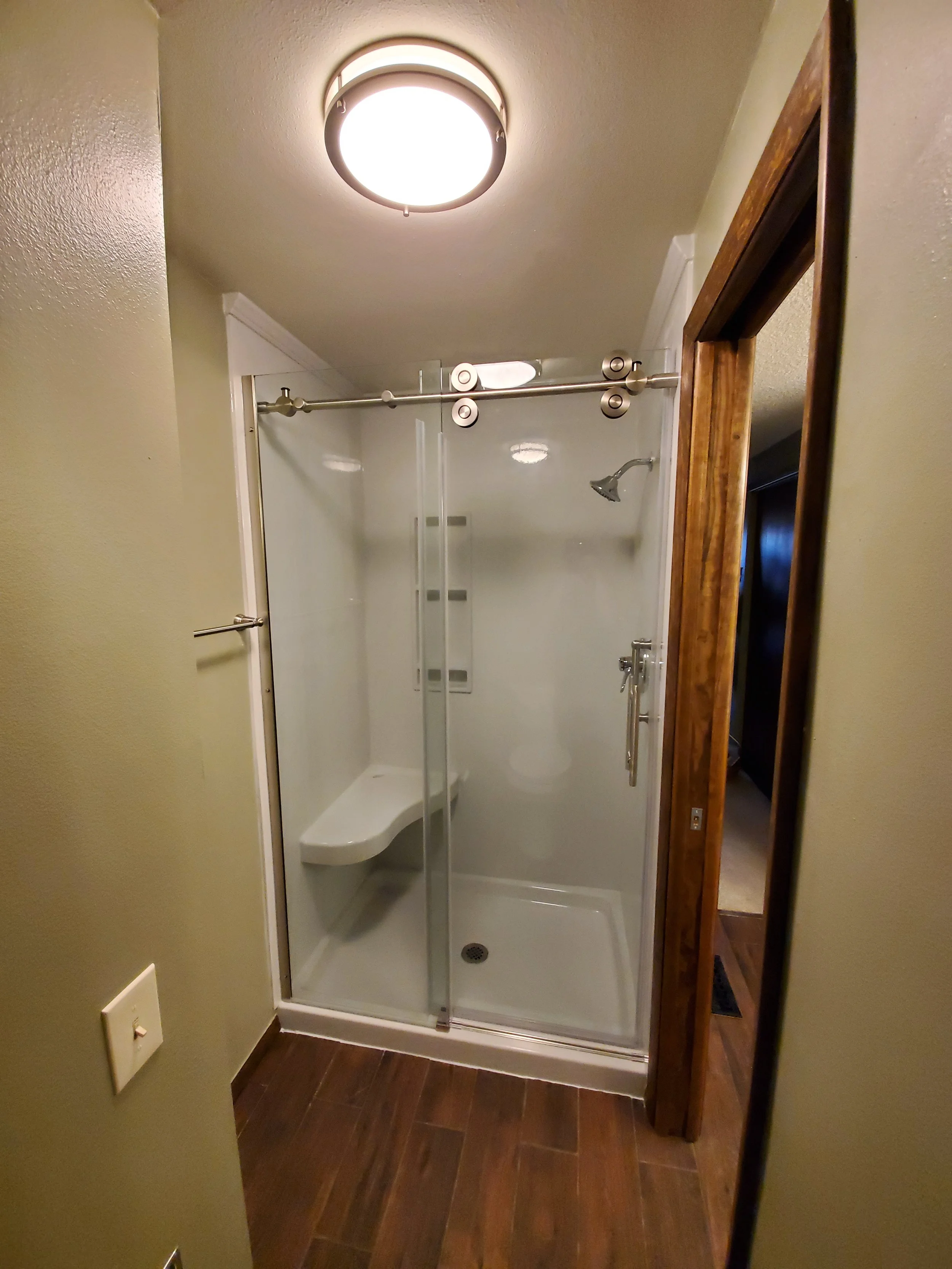 Small bathroom with a glass shower enclosure, wood trim, and wood flooring, with a ceiling light fixture.