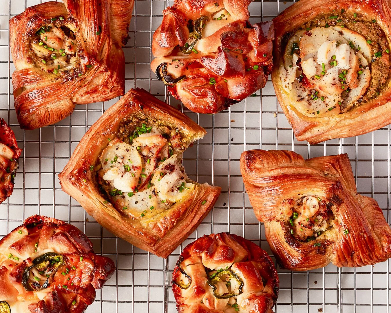 Various freshly baked savory pastries topped with herbs, placed on a wire cooling rack.
