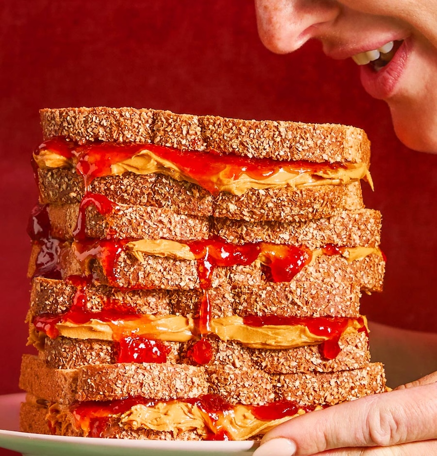 A person is about to eat a large sandwich with multiple slices of whole grain bread, peanut butter, and jelly.