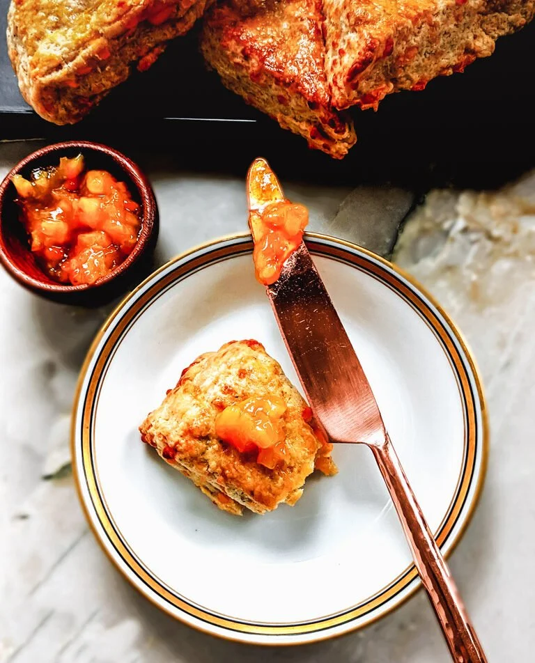 A plate with a piece of food topped with sauce, a small bowl of salsa, and a large piece of bread in the background.