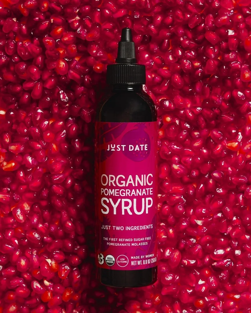 A bottle of organic pomegranate syrup placed on a bed of fresh pomegranate seeds.